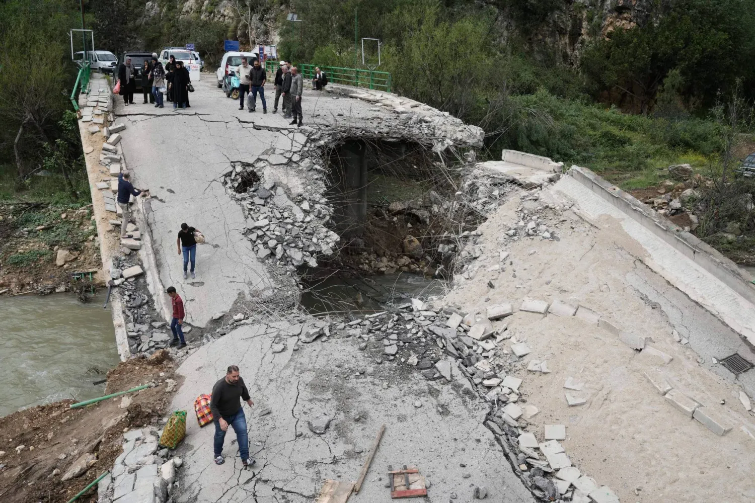 Lübnan'ın güneyindeki Tayr False köyünde yerinden edilmiş insanlar, dün evlerine dönerken yıkılmış bir köprüden geçiyorlar. (AP)