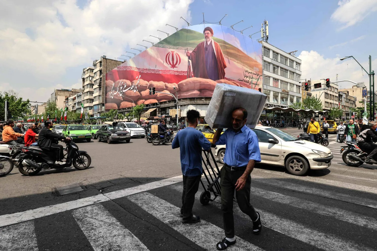 رجل يحمل طرداً على كتفه يمر أمام لوحة إعلانية كبيرة تصور المرشد مجتبى خامنئي في أحد شوارع طهران الاثنين (أ.ف.ب)