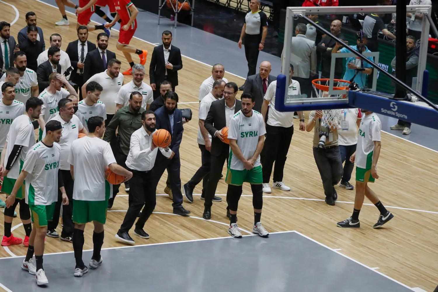 الرئيس السوري أحمد الشرع (وسط الصورة إلى اليسار) يسدد رمية حرة قبل مباراة ودية بين المنتخبين السوري واللبناني في حفل إعادة افتتاح صالة الفيحاء لكرة السلة بدمشق (أ.ب)