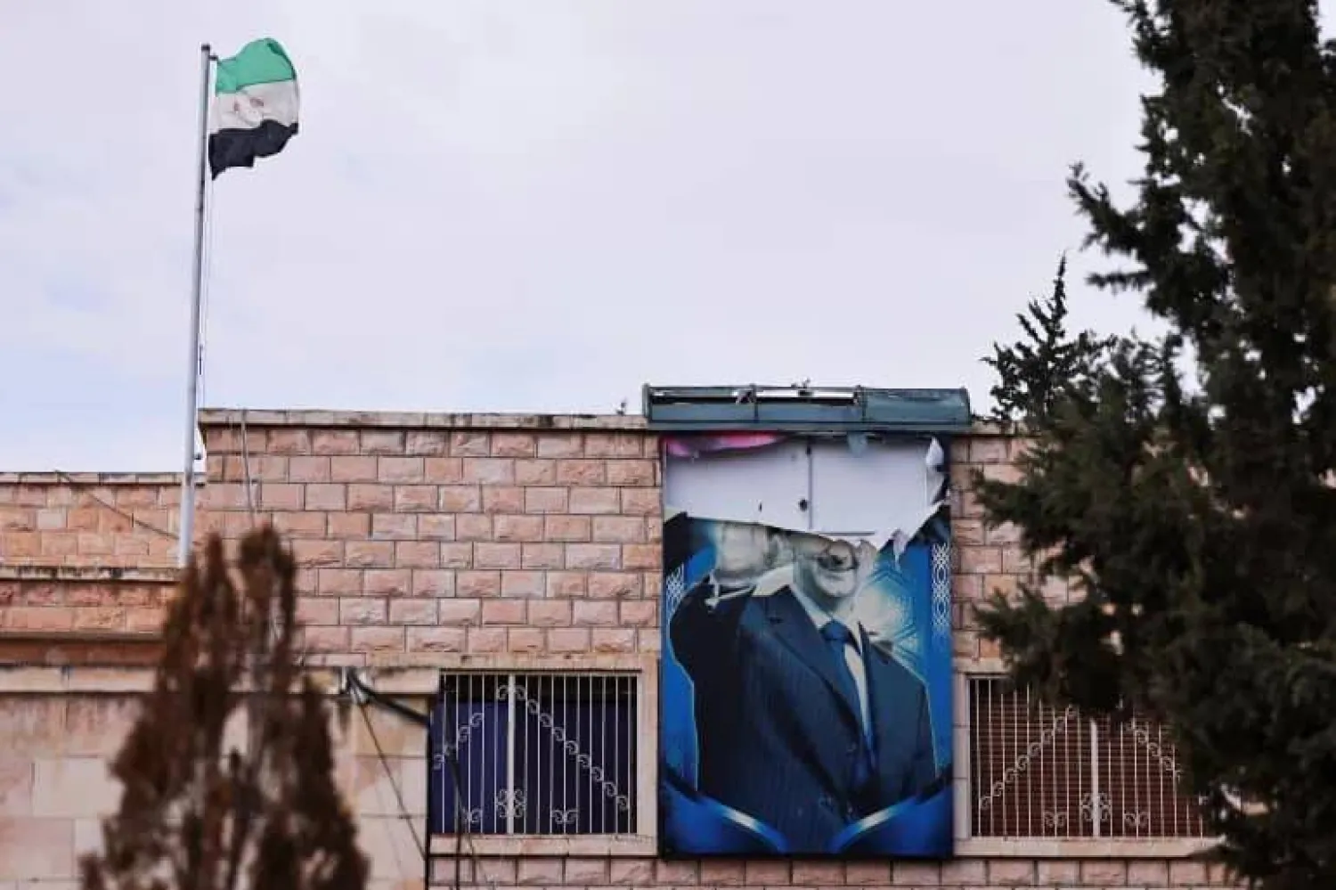 صورة ممزقة لبشار الأسد وقد علق بالقرب منها العلم السوري الجديد في درعا 27 ديسمبر 2024 (رويترز)