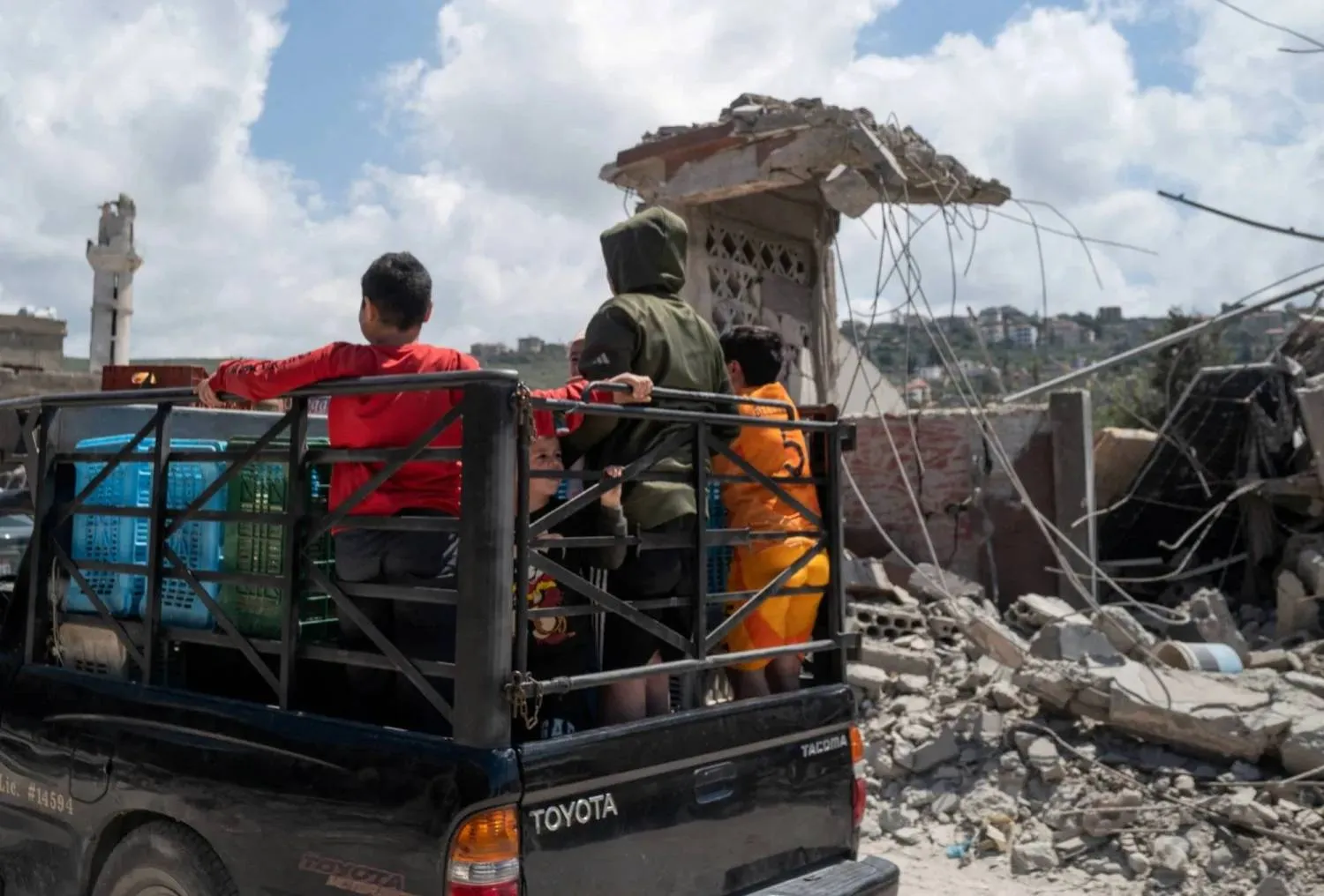 Children stand on a pickup truck as they pass damaged buildings after an Israeli airstrike in the southern Lebanese town of Mansouri (Reuters)