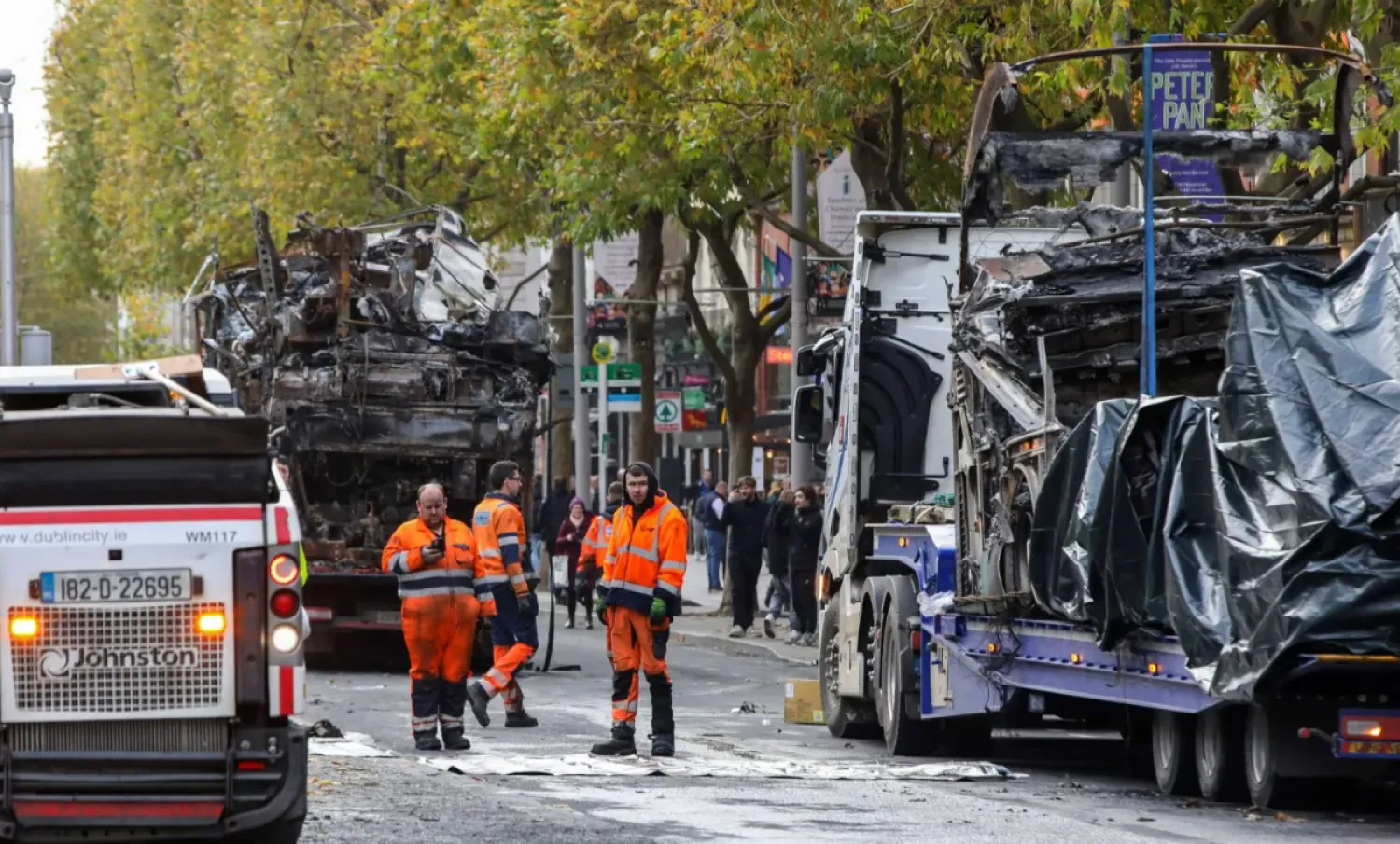 Workers clear debris from the road as the shells of burnt out buses wait to be removed from O'Connell Street in Dublin on November 24, 2023, following a night of protests. (Photo by PAUL FAITH / AFP)
