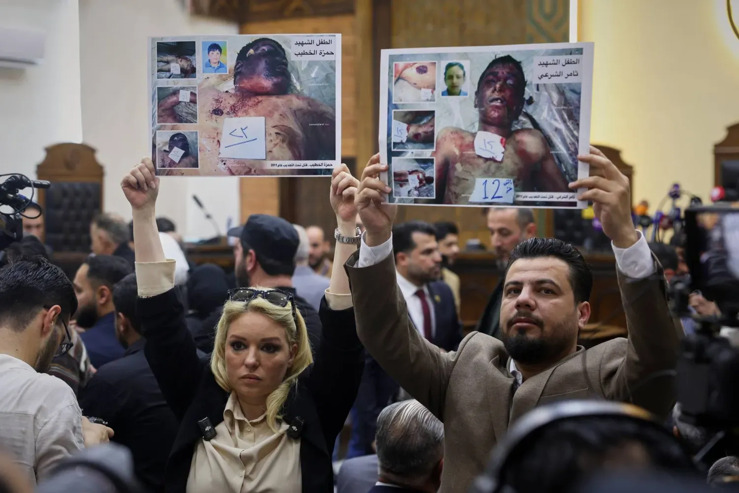 Beşşar Esed döneminde Dera'da Siyasi Güvenlik Şubesi Başkanı olan Atıf Necip'in ilk duruşması sırasında Suriye ayaklanmasının başlarında hayatını kaybeden çocukların fotoğraflarını kaldıran aktivistler (AP)