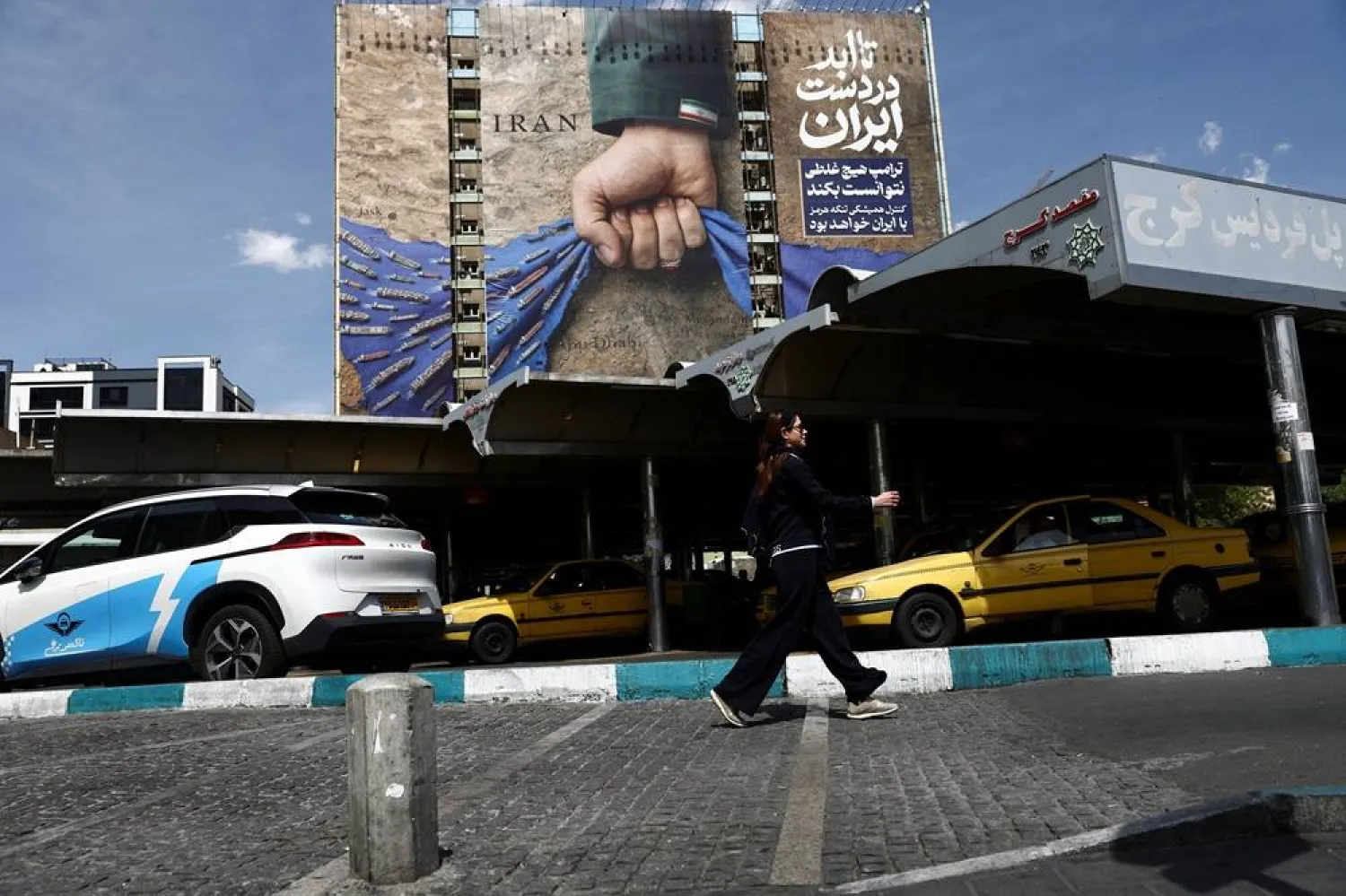 A woman walks past a billboard with a graphic design about the Strait of Hormuz on a building, amid a ceasefire between US and Iran, in Tehran, Iran, April 27, 2026. Majid Asgaripour/WANA (West Asia News Agency) via Reuters 
