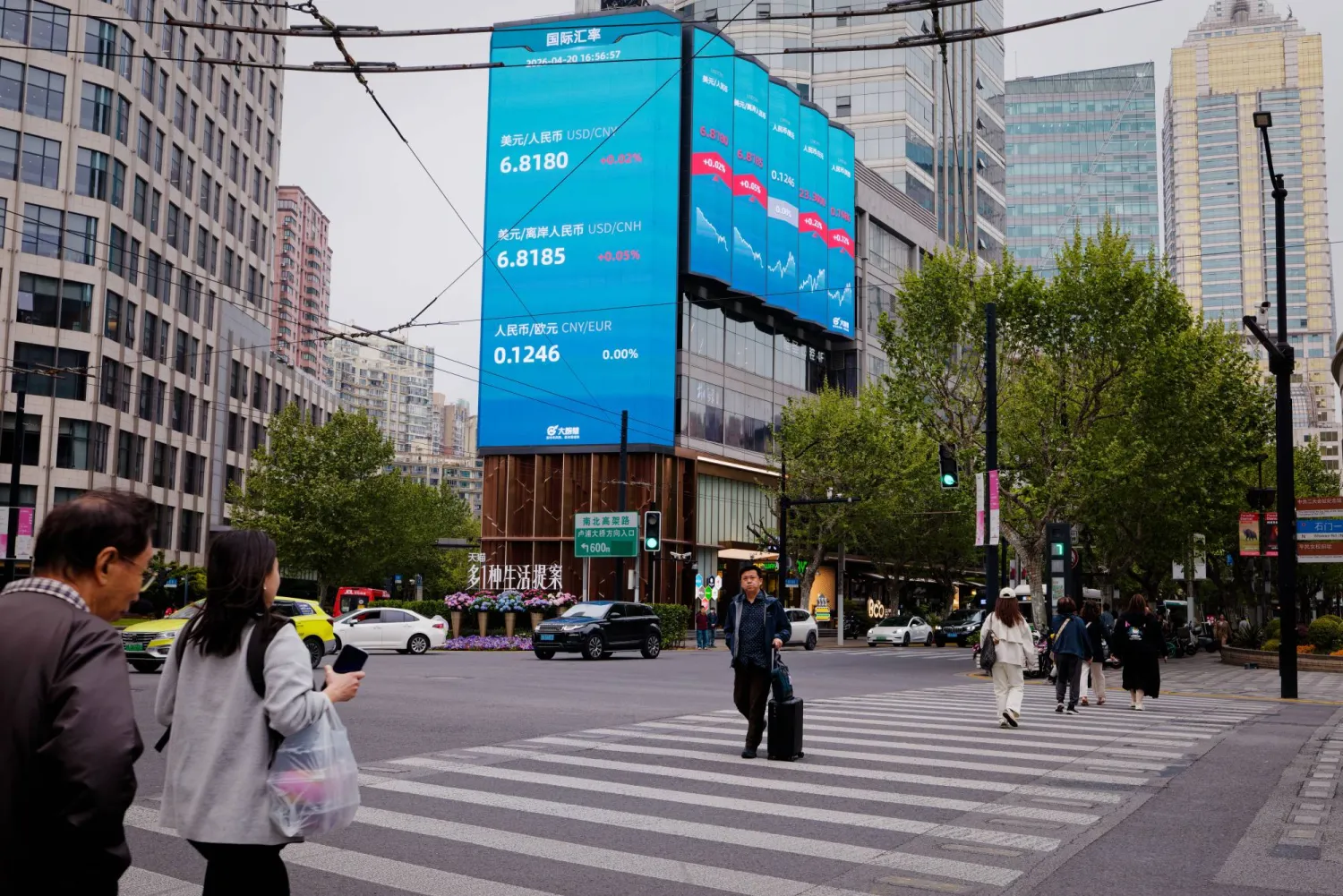 مشاة في أحد شوارع مدينة شنغهاي الصينية بينما تبدو خلفهم شاشة عملاقة تعرض حركة الأسهم (إ.ب.أ)