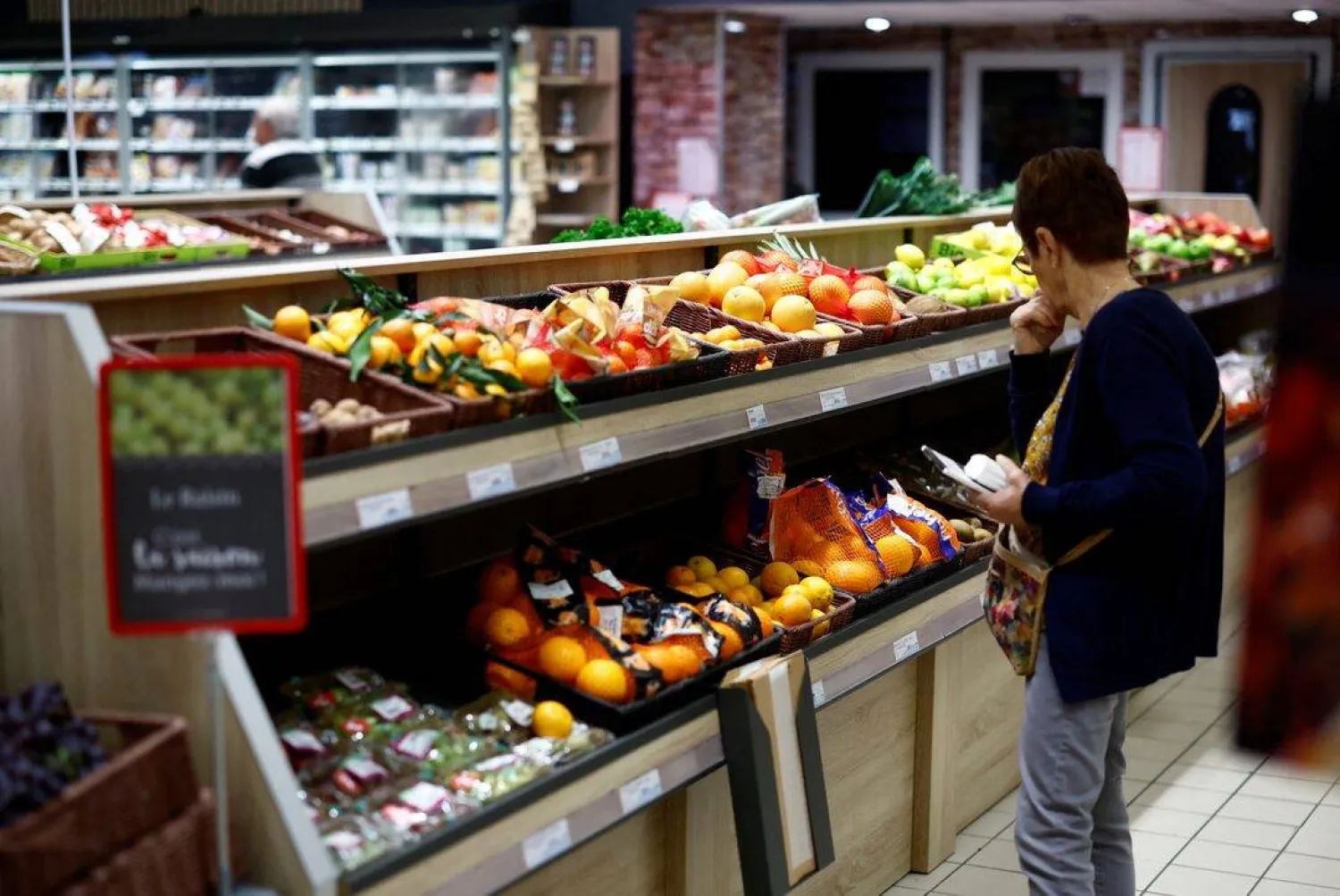 متسوقة بقسم الفواكه والخضراوات داخل أحد المتاجر الكبرى في شانفيري بفرنسا (رويترز)