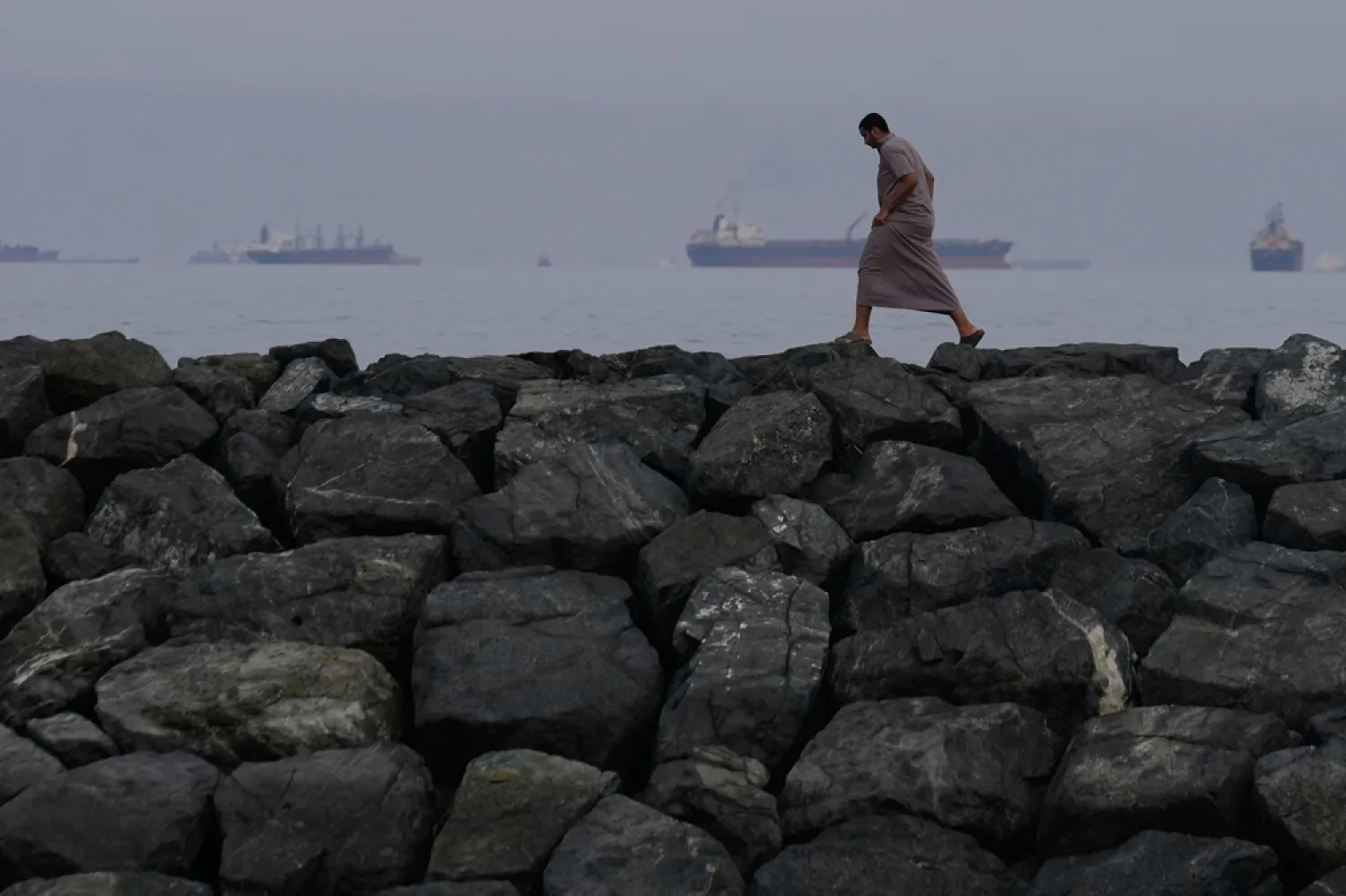 A man walks along the shore as oil tankers and cargo ships line up in the Strait of Hormuz, seen from Khor Fakkan, United Arab Emirates, March 11, 2026. (AP)