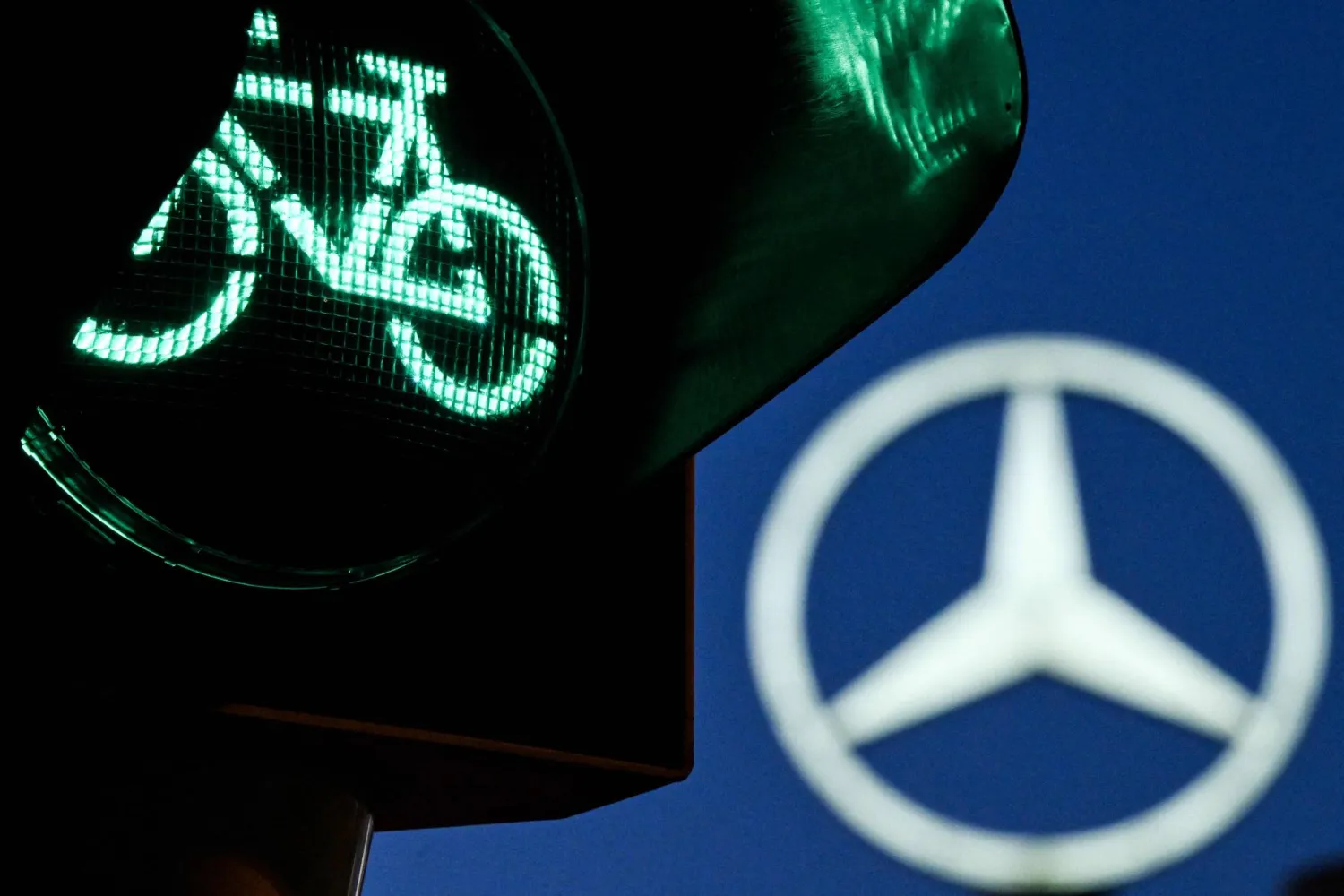 A traffic light for cyclists is pictured in front of a giant logo of German automotive brand Mercedes-Benz is seen atop a Mercedes dealership in Offenbach, western Germany, on April 29, 2026. (AFP)