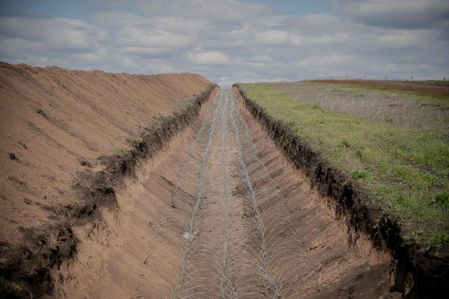 This photograph shows a barbed wire defense line running across a field at an undisclosed location in the Kharkiv region, eastern Ukraine, on May 1, 2026, amid the Russian invasion of Ukraine. (AFP) 