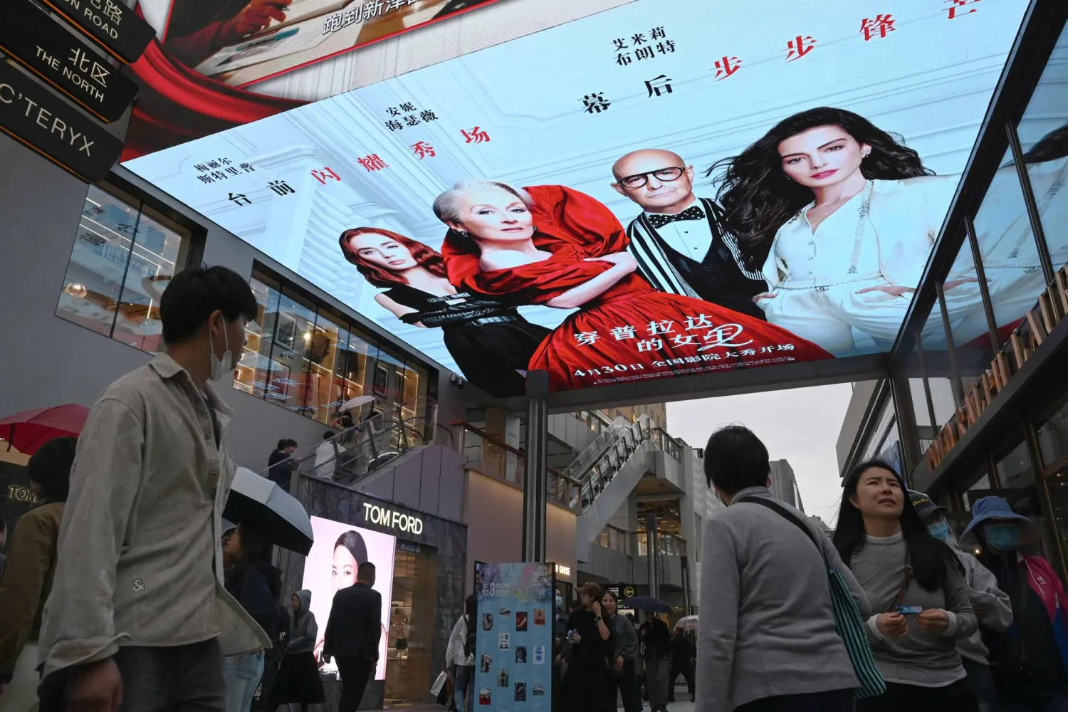 People walk below an electronic billboard advertising the movie "The Devil Wears Prada 2" at a shopping mall in Beijing on May 2, 2026, on the second day of a five-day national May Day holiday. (Photo by GREG BAKER / AFP)