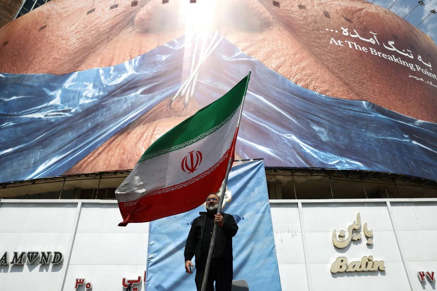 A man holds an Iranian flag near an anti-US billboard depicting US President Donald Trump and the Strait of Hormuz, in Tehran, Iran, May 2, 2026. Majid Asgaripour/WANA (West Asia News Agency) via Reuters