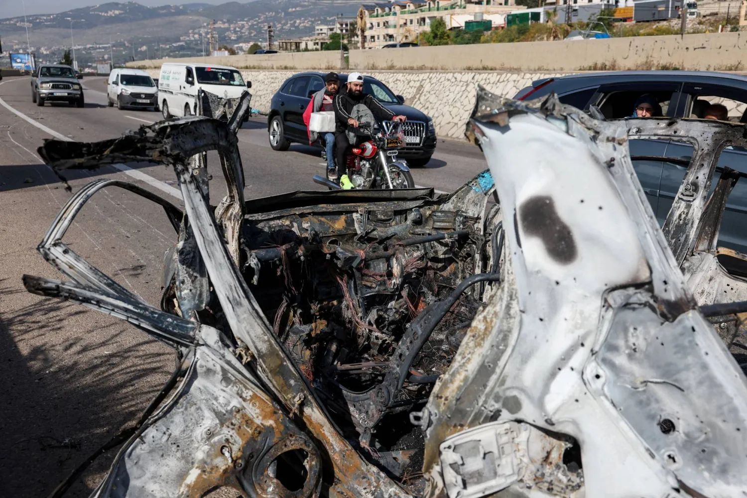 People ride a scooter past a destroyed car that was targeted by an Israeli strike, in Saadiyat, Lebanon, May 9, 2026. REUTERS/Mohamed Azakir 