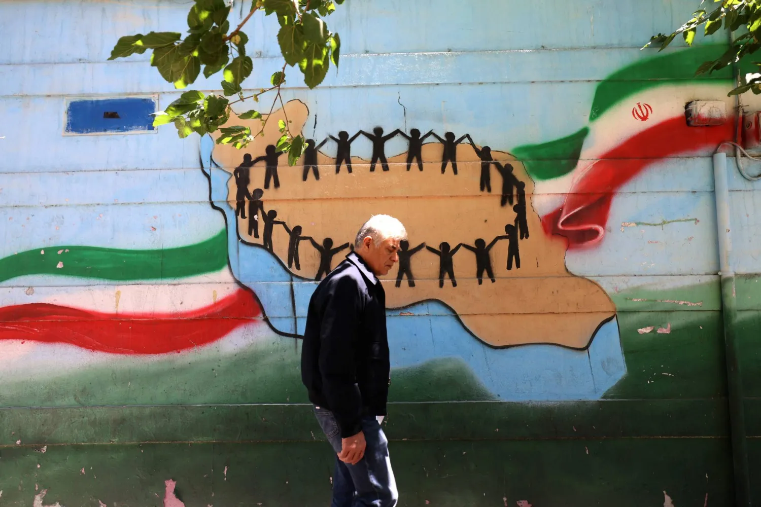 An Iranian man walks past the map of Iran, with its citizens holding hands, painted on a wall in the capital Tehran on May 9, 2026. (AFP)