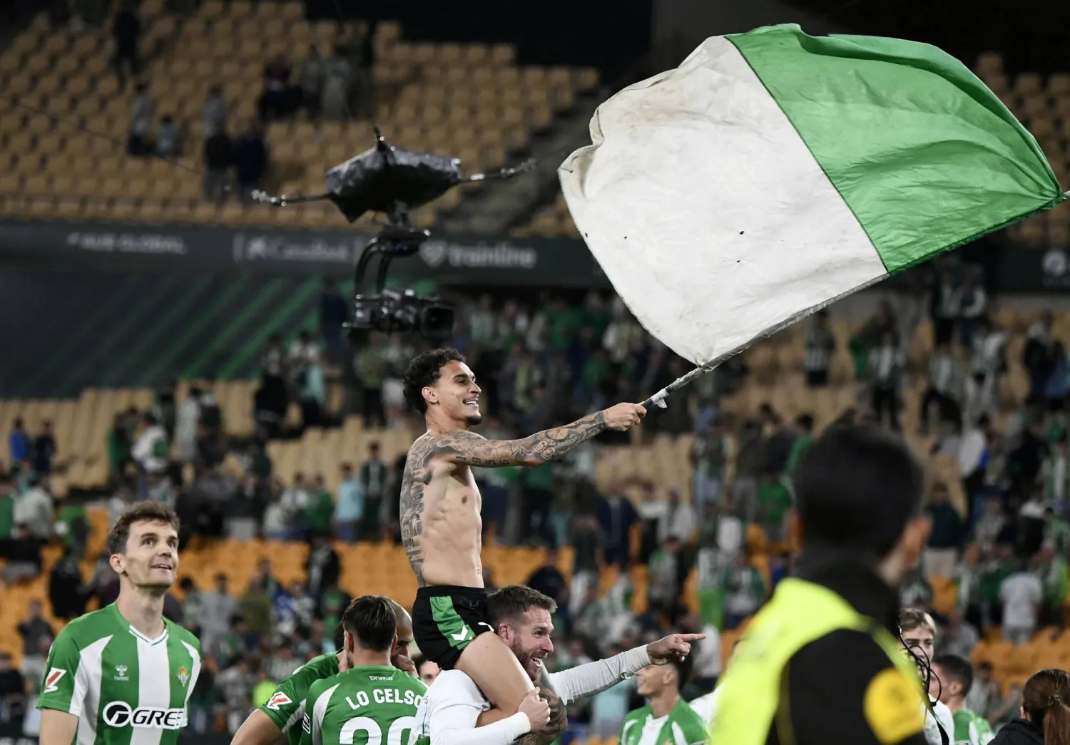 البرازيلي أنتوني نجم ريال بيتيس يلوّح بعلم الفريق احتفالاً بالتأهل لدوري الأبطال (أ.ف.ب)