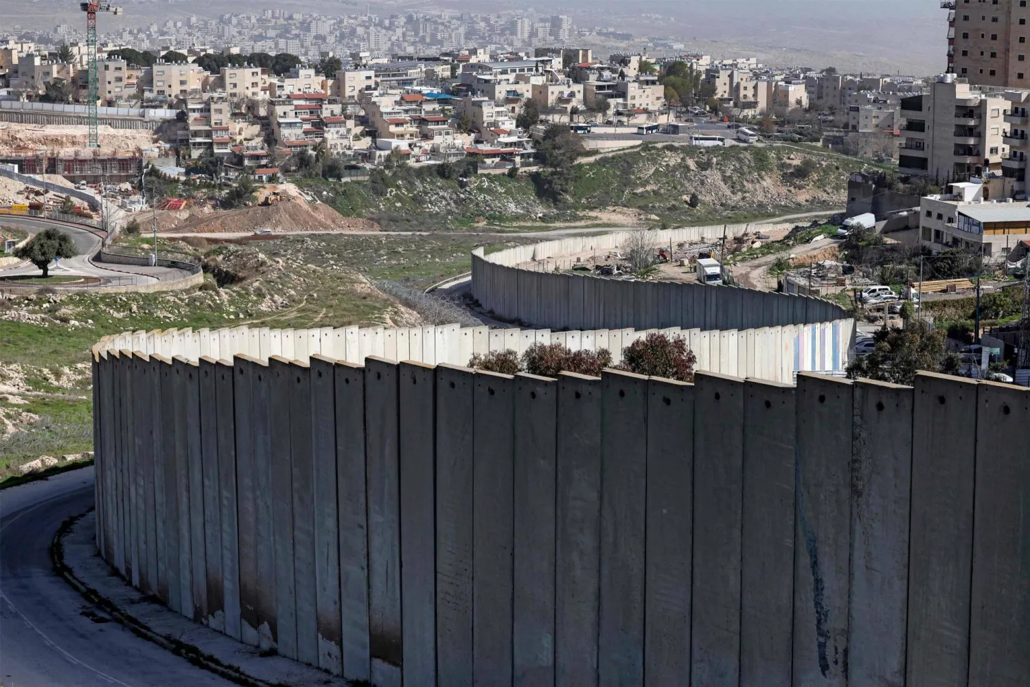 صورة لمستوطنة بسغات زئيف الإسرائيلية (يسار) التي بنيت في ضاحية من ضواحي القدس الشرقية ذات الأغلبية العربية خلف جدار الفصل الإسرائيلي في 16 فبراير الماضي (أ.ف.ب)