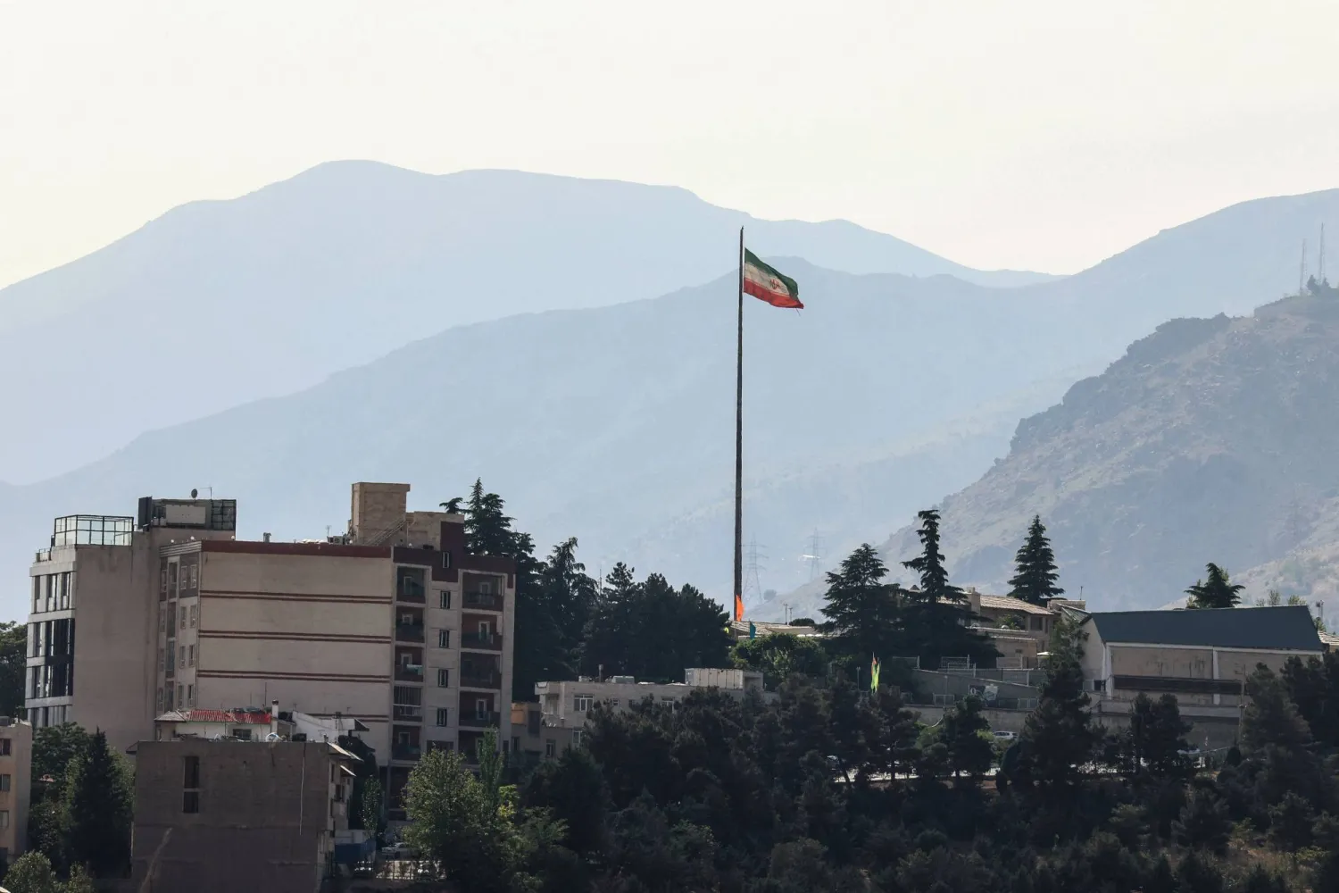 The Iran flag flutters from a tall flagpole over high-rise buildings in northern Tehran on May 12, 2026. (AFP)