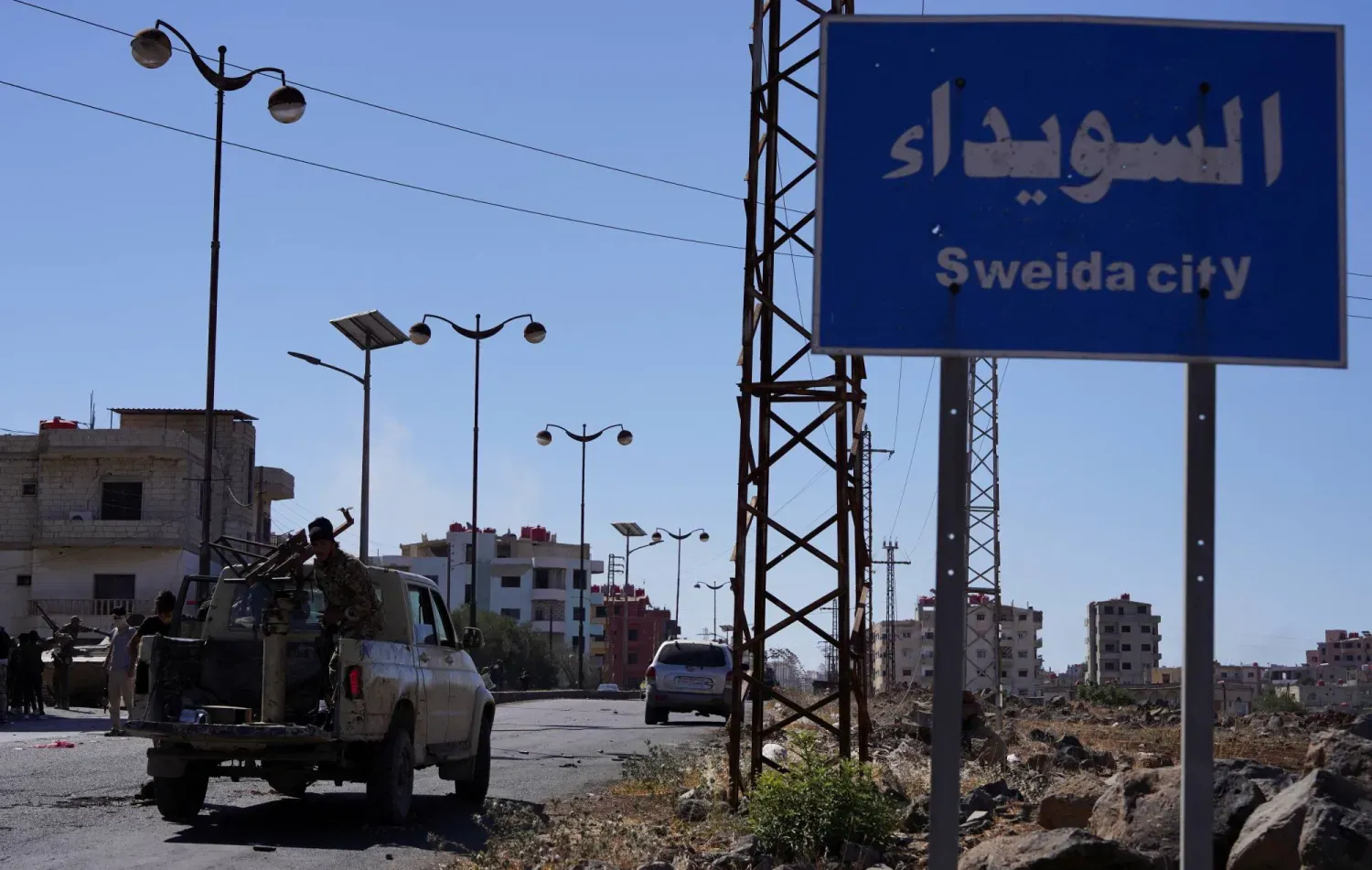 Suveyda yazılı tabelanın yanından geçen Suriye güvenlik güçleri (Reuters)