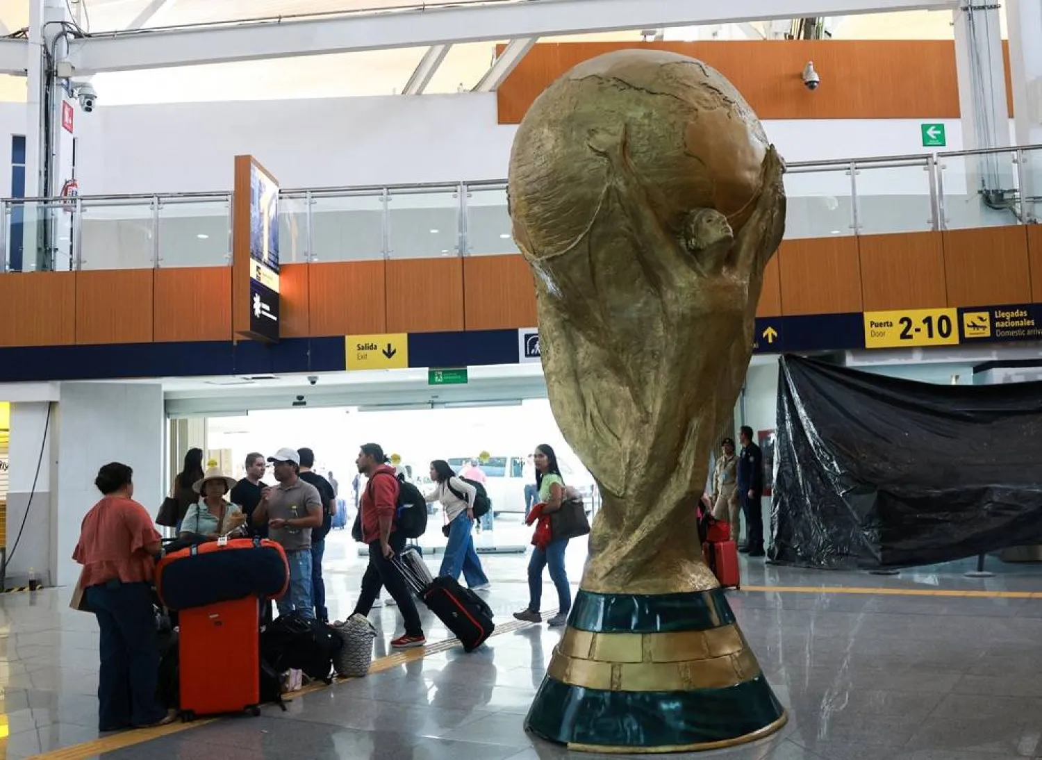  Passengers stand beside a giant replica of the World Cup trophy displayed at Mexico City International Airport, ahead of the World Cup starting on June 11, in Mexico City, Mexico, May 15, 2026. (Reuters)
