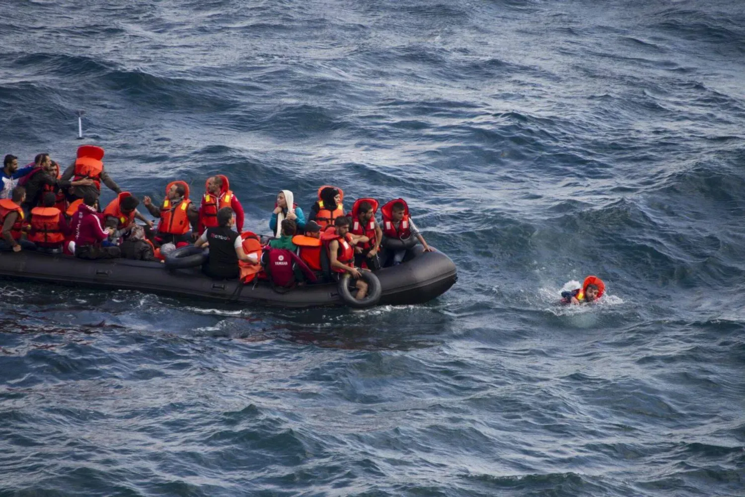 Yunanistan'ın Lesbos adası kıyıları yakınlarında, Türk kıyılarından Ege Denizi'nin bir bölümünü geçmekte olan ve göçmenlerle dolu lastik botun yanında yüzen bir göçmen görülüyor (Reuters- Arşiv)