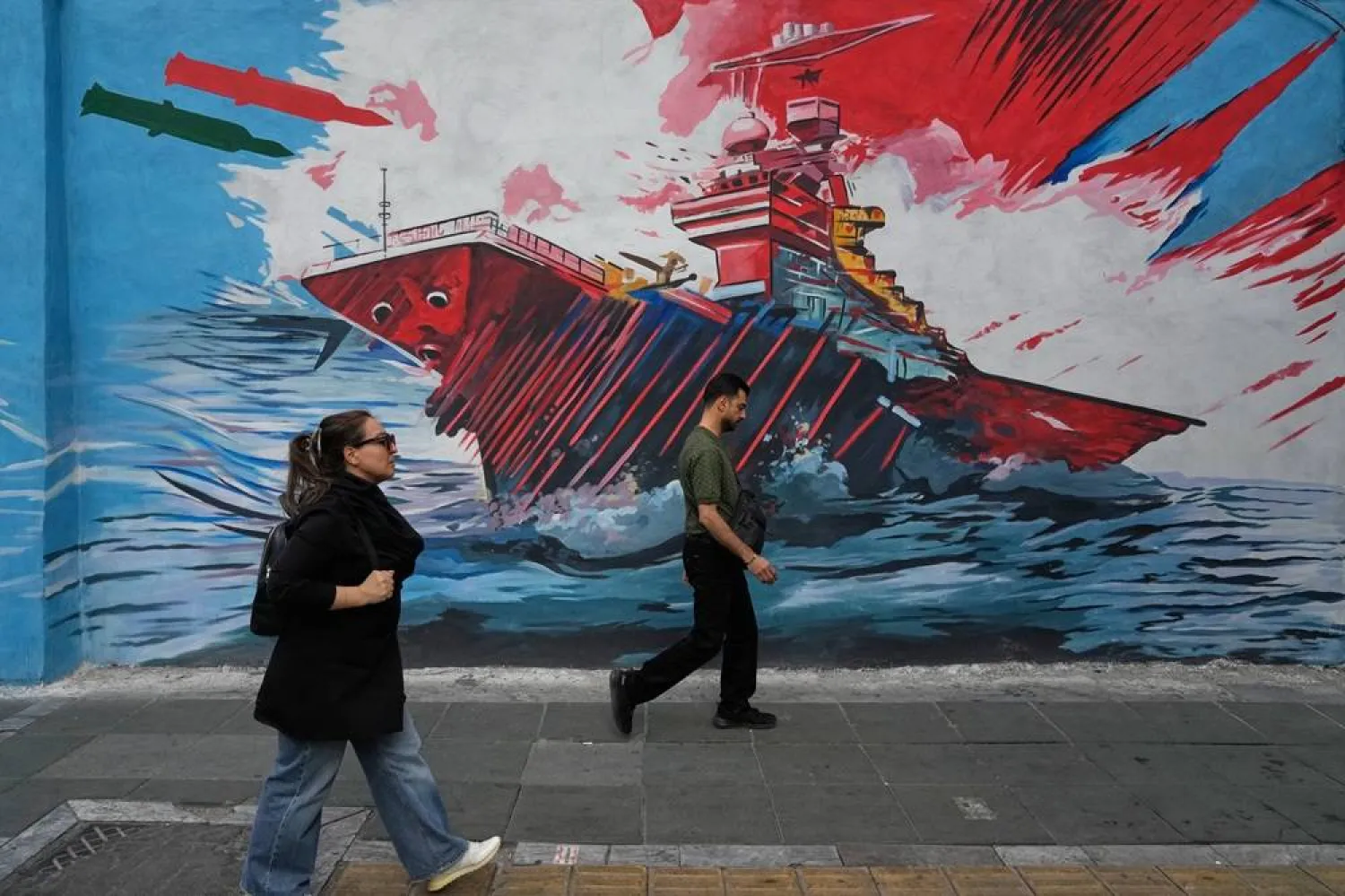  People walk past a mural depicting a US aircraft carrier under missile attack in downtown Tehran, Iran, Sunday, May 17, 2026. (AP) 