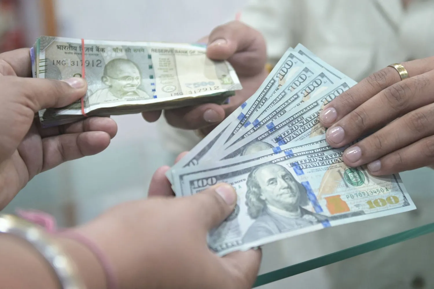 أشخاص يحملون أوراقاً نقدية من الدولار والروبية الهندية (أ.ف.ب)