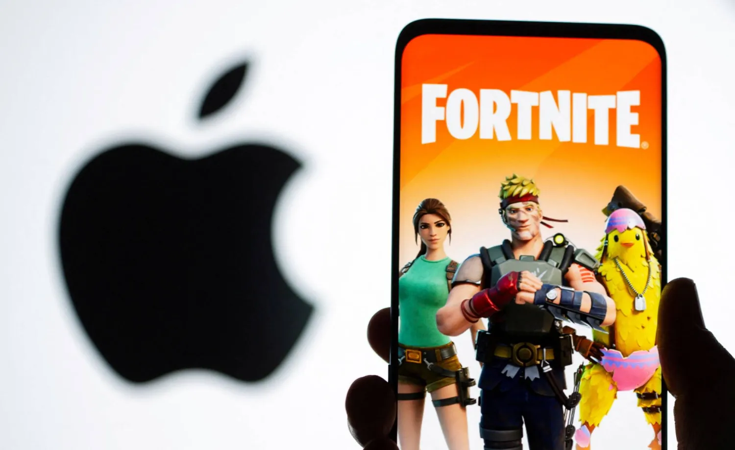 صورة ترتبط بلعبة «فورتنايت» تظهر على شاشة هاتف ذكي أمام شعار «أبل» (رويترز)