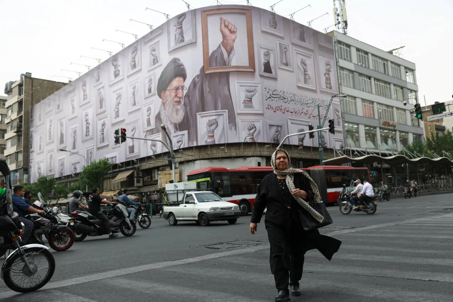 سيدة تسير في أحد شوارع طهران وفي الخلفية لافتة عملاقة تحمل صورة المرشد السابق علي خامنئي (رويترز)