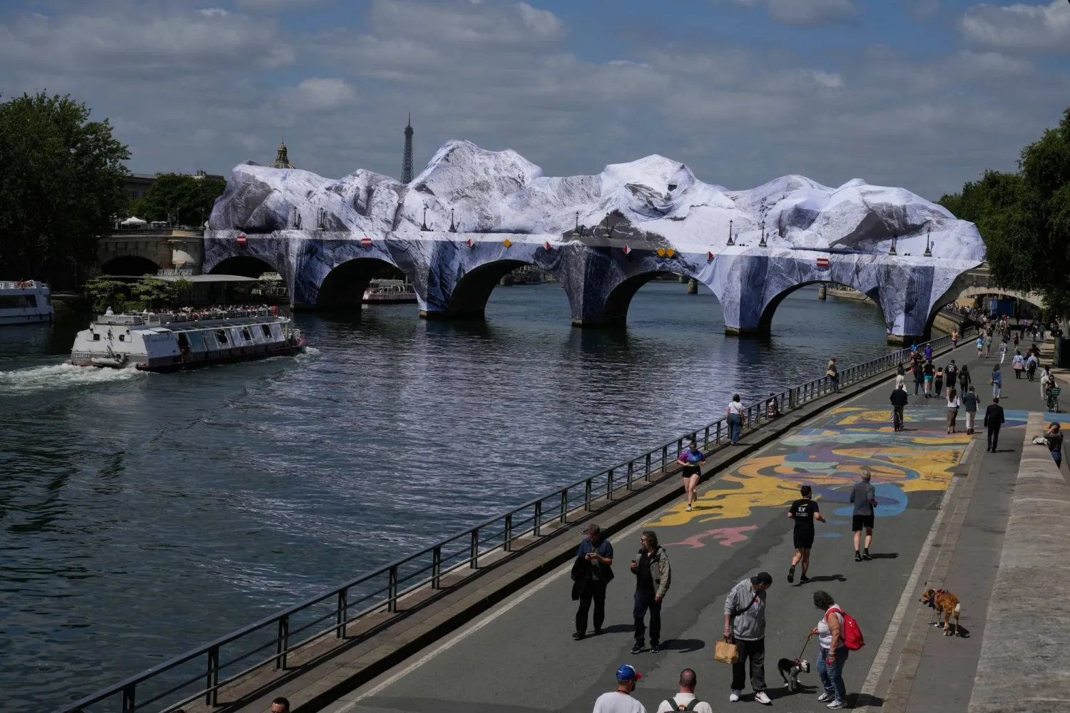 People walk along the Seine river next to "The Pont Neuf Cave," an inflated art installation by French street artist JR, on Paris' oldest bridge, the Pont Neuf, Thursday, May 21, 2026, which will be open to the public from June 6-28. (AP Photo/Michel Euler)