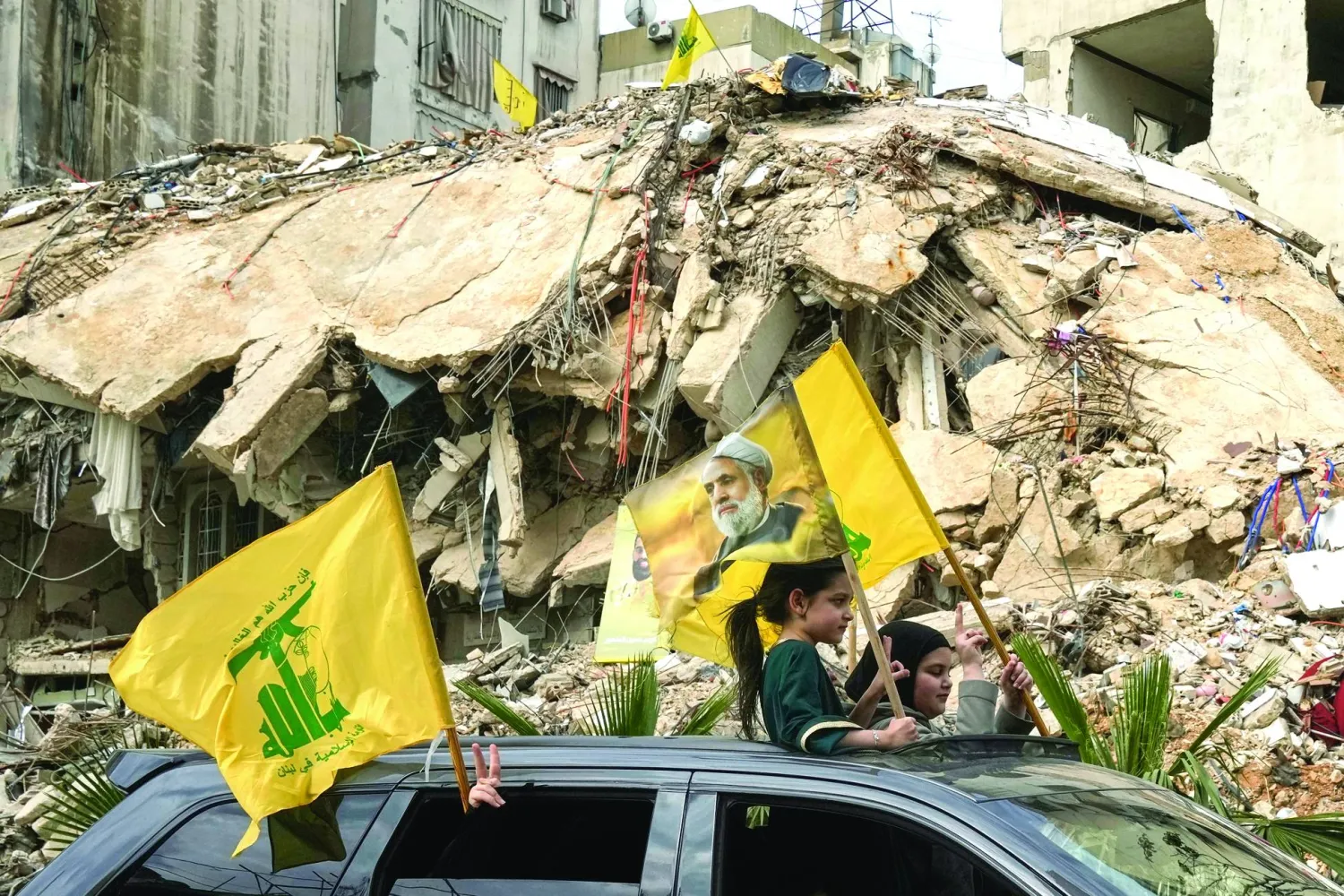 نازحون عائدون إلى ضاحية بيروت الجنوب يحملون علم «حزب الله» وصورة أمين عام الحزب نعيم قاسم (أ.ب)