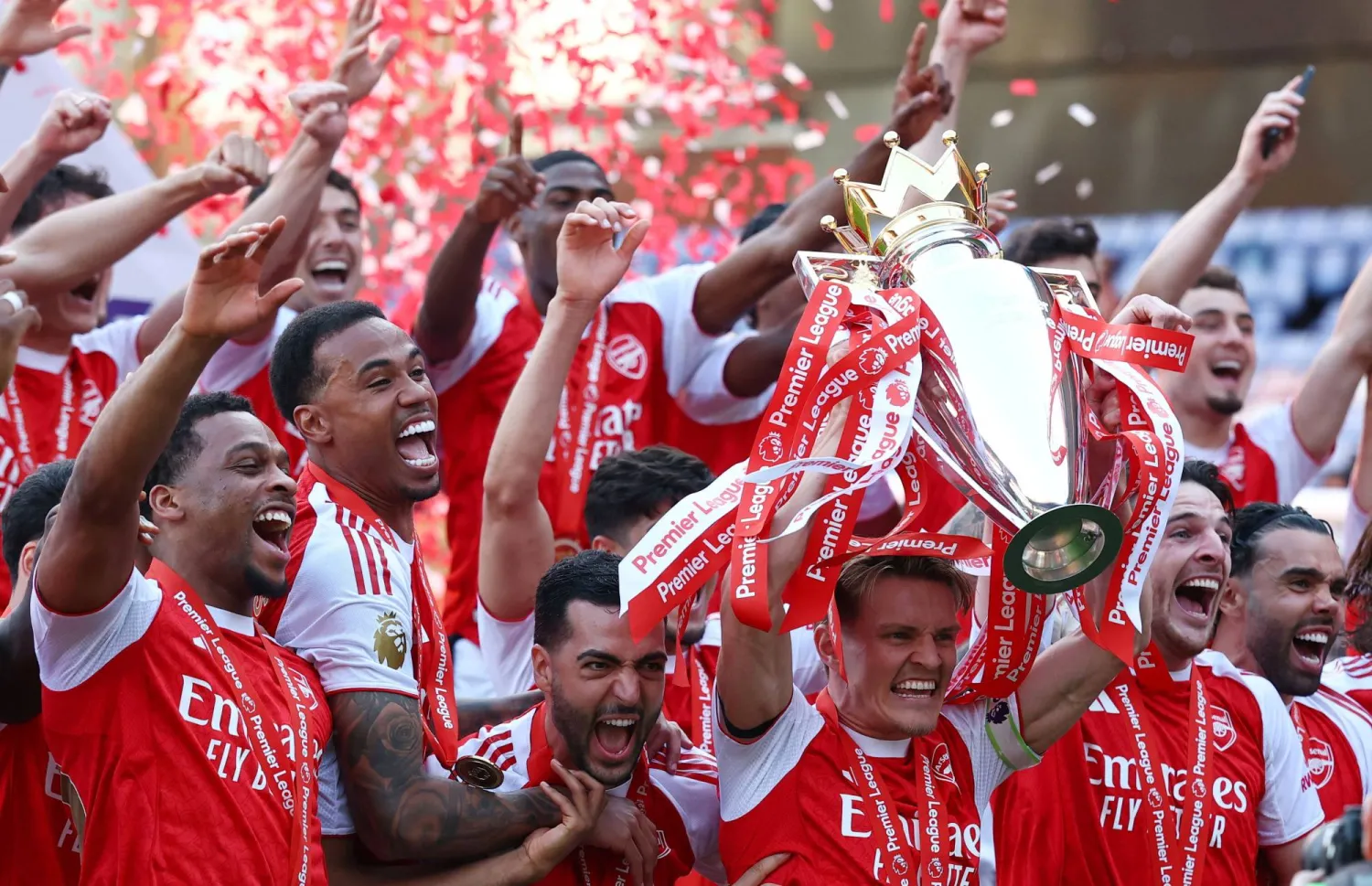 مارتن أوديغارد يرفع الكأس وهو يحتفل مع زملائه بعد الفوز بالدوري الإنجليزي الممتاز (رويترز)