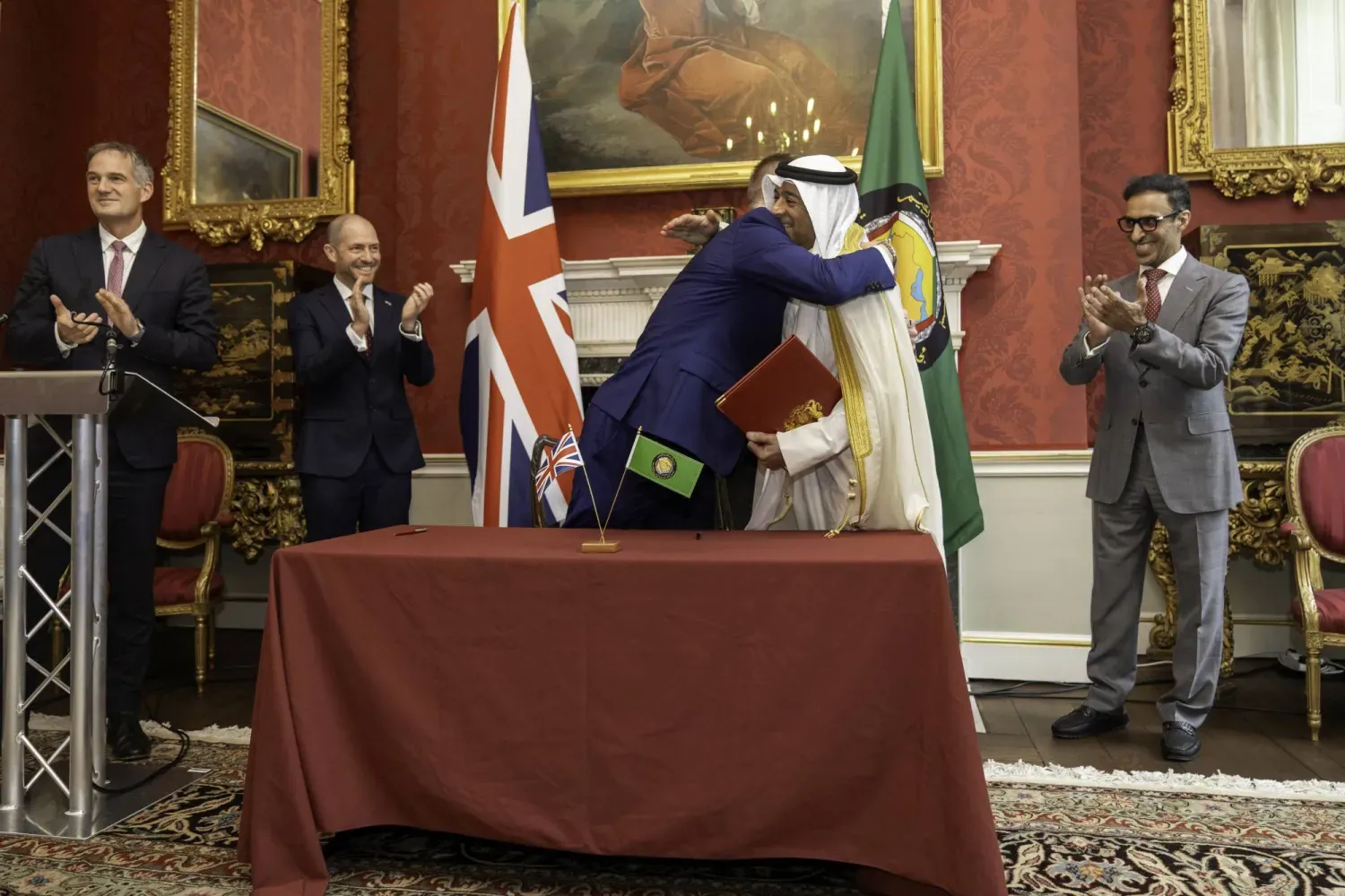 Körfez İşbirliği Konseyi (KİK) Genel Sekreteri Casim Muhammed el-Budeyvi ve Birleşik Krallık Ticaretten Sorumlu Devlet Bakanı Chris Bryant, Londra’da anlaşmayı imzaladıktan sonra müzakerecilerin alkışları eşliğinde birbirlerine sarıldılar. (Birleşik Krallık Ekonomi Bakanlığı)