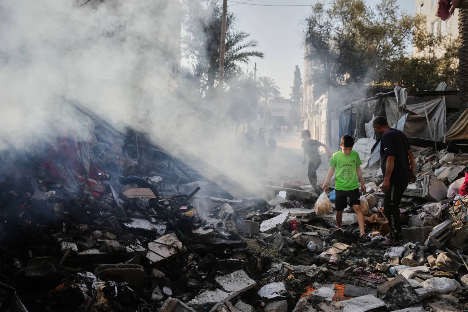 فلسطينيون يمرون وسط أنقاض منزل لعائلة الكرد دمرته غارة إسرائيلية على دير البلح (أ.ب)