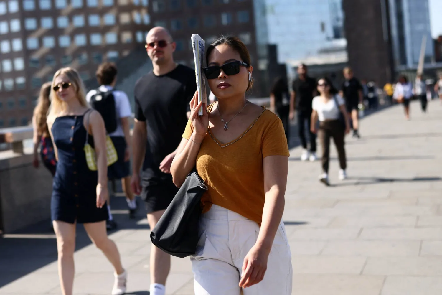 A woman shields herself from the sun with a newspaper as she crosses London Bridge during a heatwave in London, Britain, May 26, 2026. REUTERS/Jack Taylor