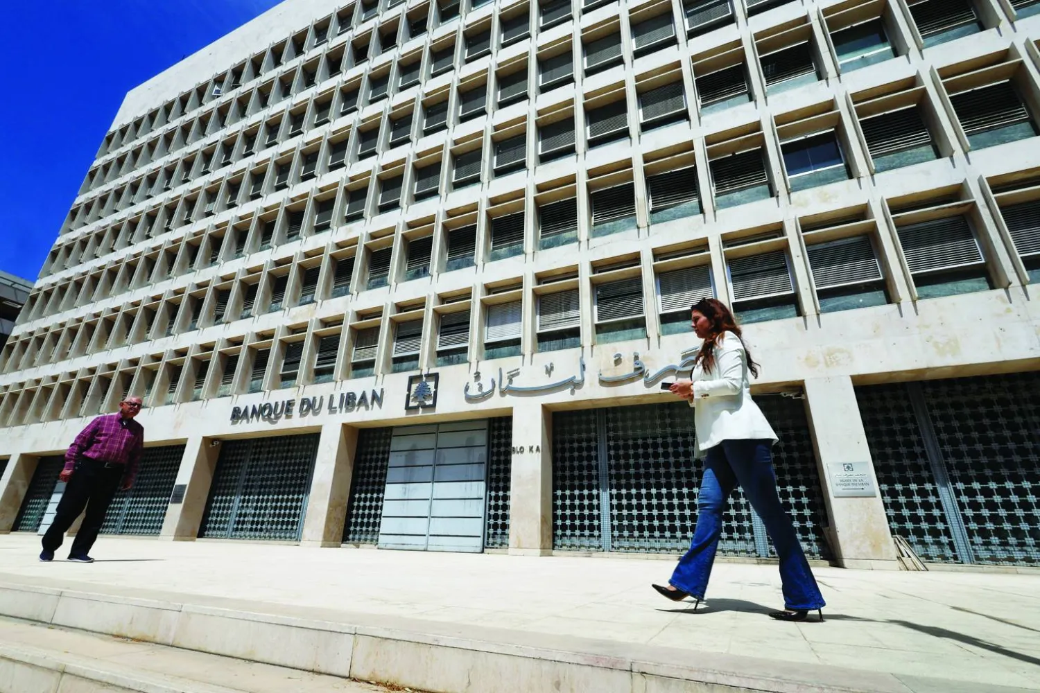أشخاص يسيرون أمام مقر مصرف لبنان المركزي في منطقة الحمراء ببيروت (رويترز)