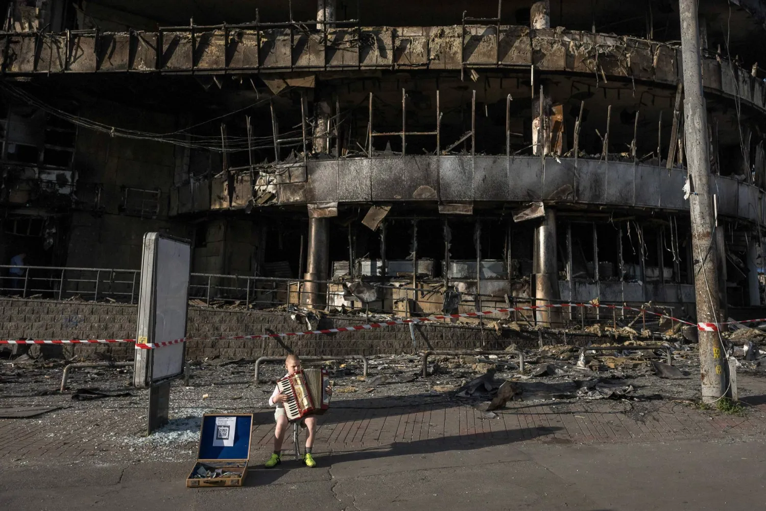 A boy plays the accordion in front of a shopping center damaged by Russian strikes in Kyiv on May 25, 2026, amid the Russian invasion of Ukraine. (AFP) 