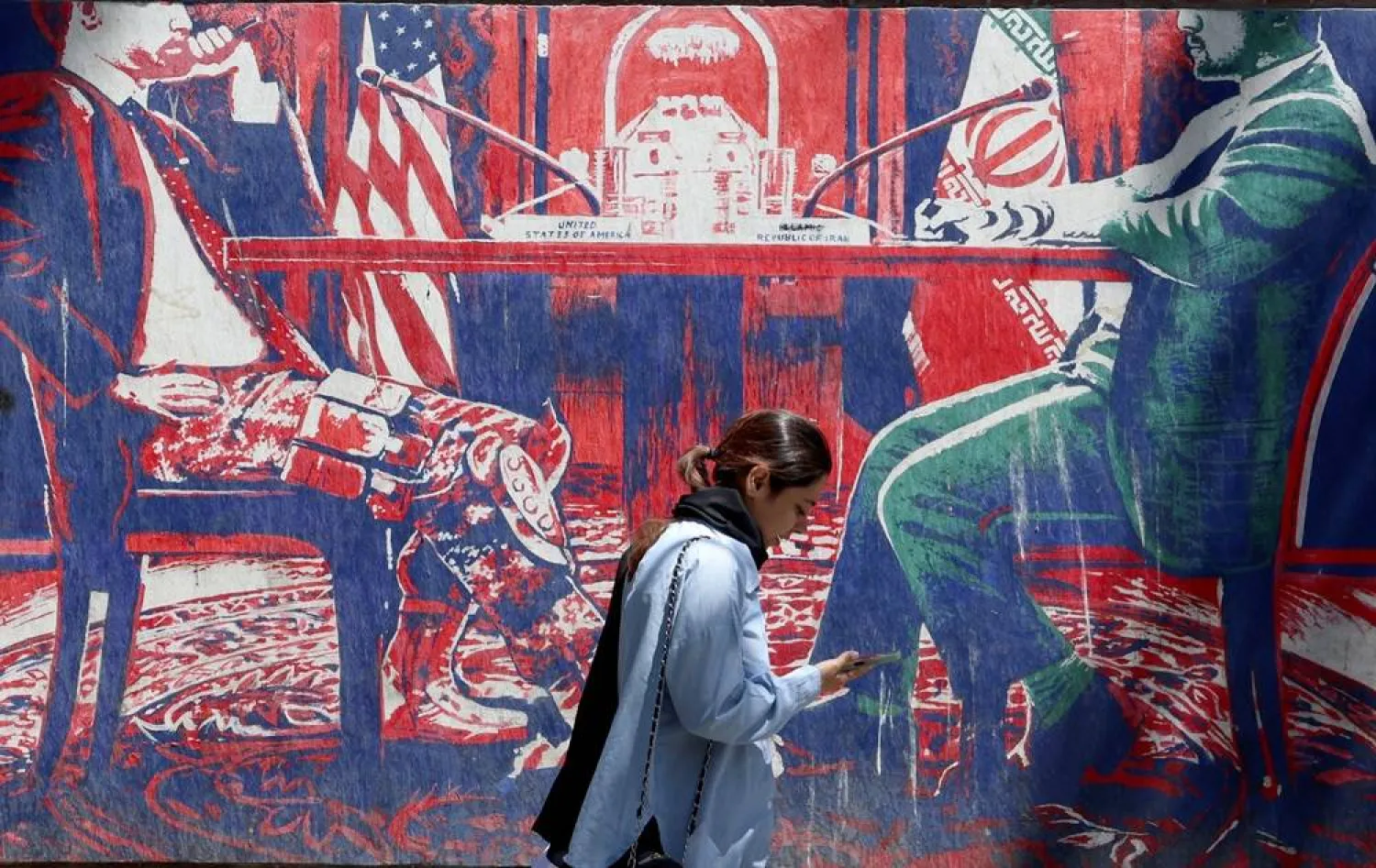 An Iranian girl walks next to an anti-US mural depicting Iran and US negotiations at a table, near the former US Embassy in Tehran, Iran, 26 May 2026. (EPA)
