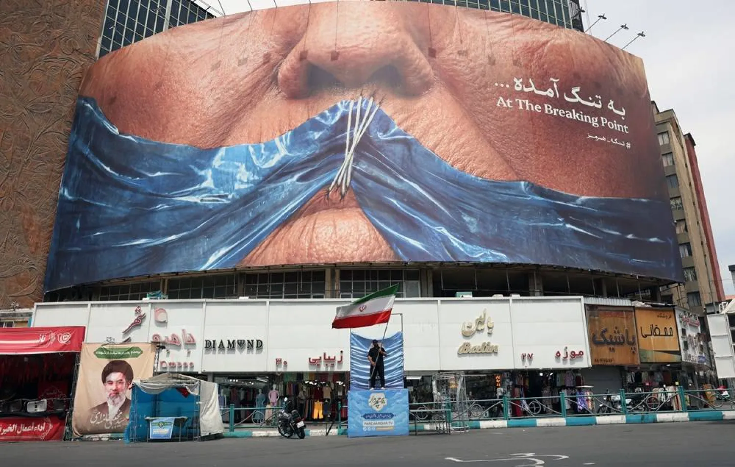 A man holds Iran’s national flag in front of a large anti-US billboard featuring US President Donald Trump and the Strait of Hormuz at Valiasr Square in Tehran, Iran, 28 May 2026. (EPA)