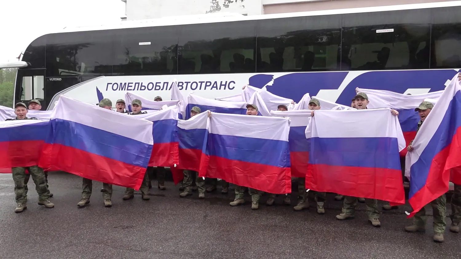 This video grab taken from a handout footage released by the Russian Defense Ministry on May 15, 2026, shows Russian prisoners of war (POWs) posing with flags in front of a bus following an exchange of prisoners at an undisclosed location in Belarus. (AFP / Russian Defense Ministry/ Handout) 