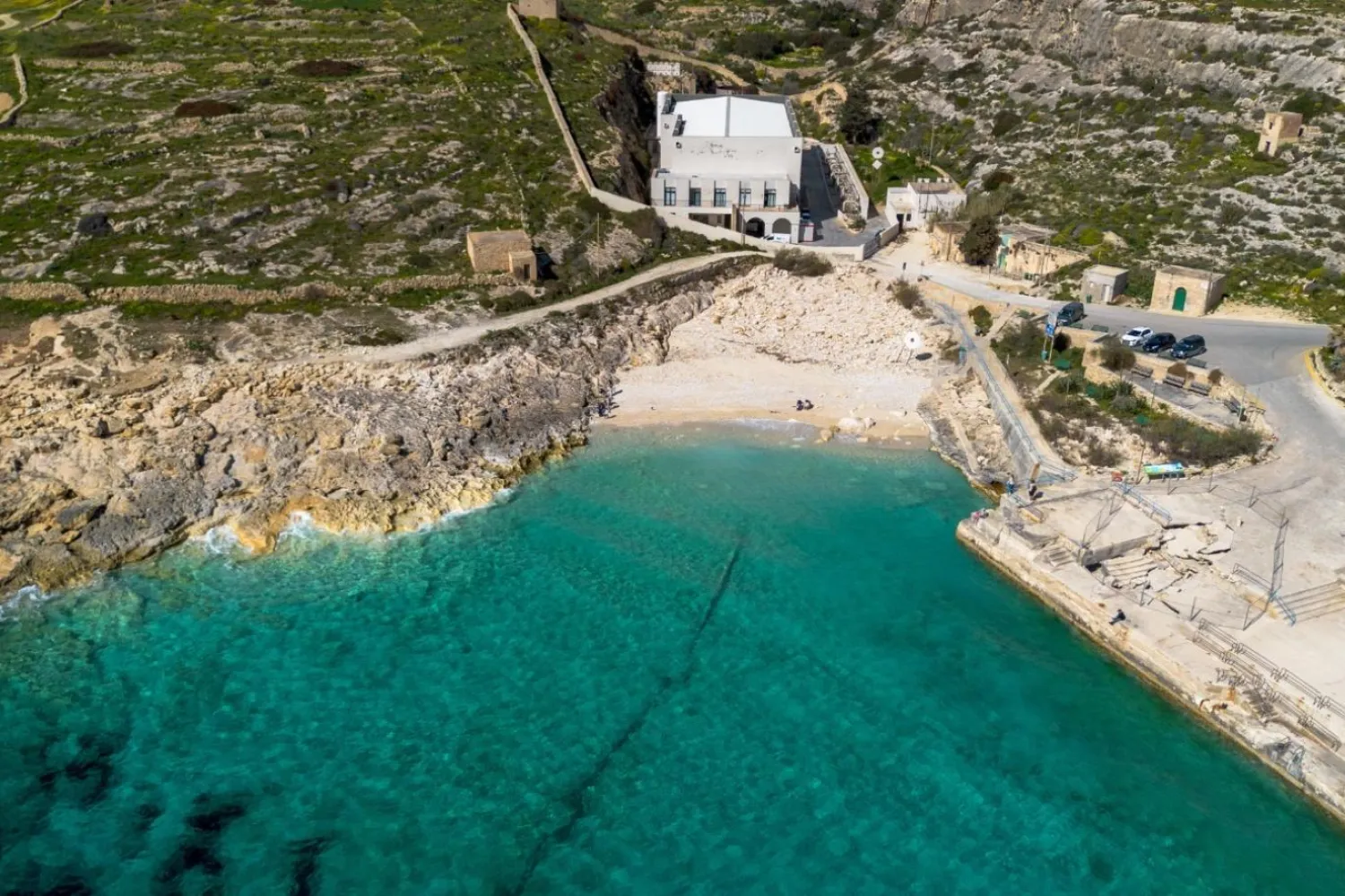 Malta'nın Gozo adasındaki Qala'da bulunan Hondoq ir Rummien ir-rummein tuzdan arındırma tesisinin, kayalık kıyı şeridinin, küçük plajın ve turkuaz Akdeniz sularında görünen açık deniz tuzlu su tahliye borusunun havadan görünümü (Hans Lucas/AFP)
