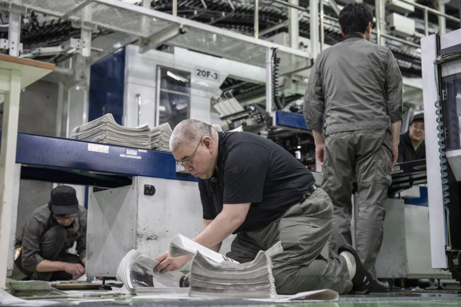 As the machine printed their work on newsprint paper, five technicians in uniform quickly flipped through the pages to check the quality. Yuichi YAMAZAKI / AFP
