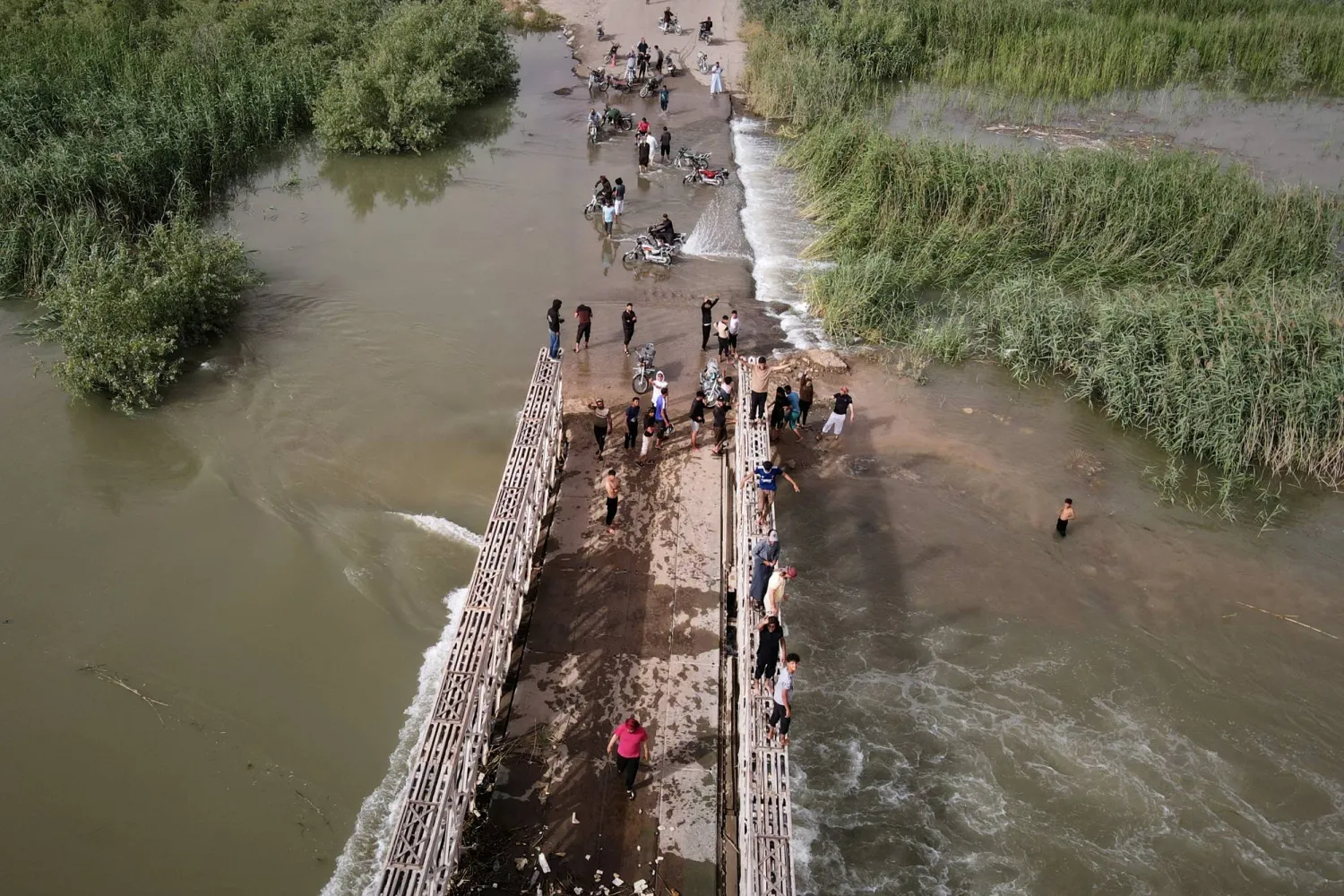People walk across and stand on a bridge damaged by overflowing waters from the Euphrates River near Deir Ezzor, Syria, Thursday, May 28, 2026. (AP Photo/Omar Albam)