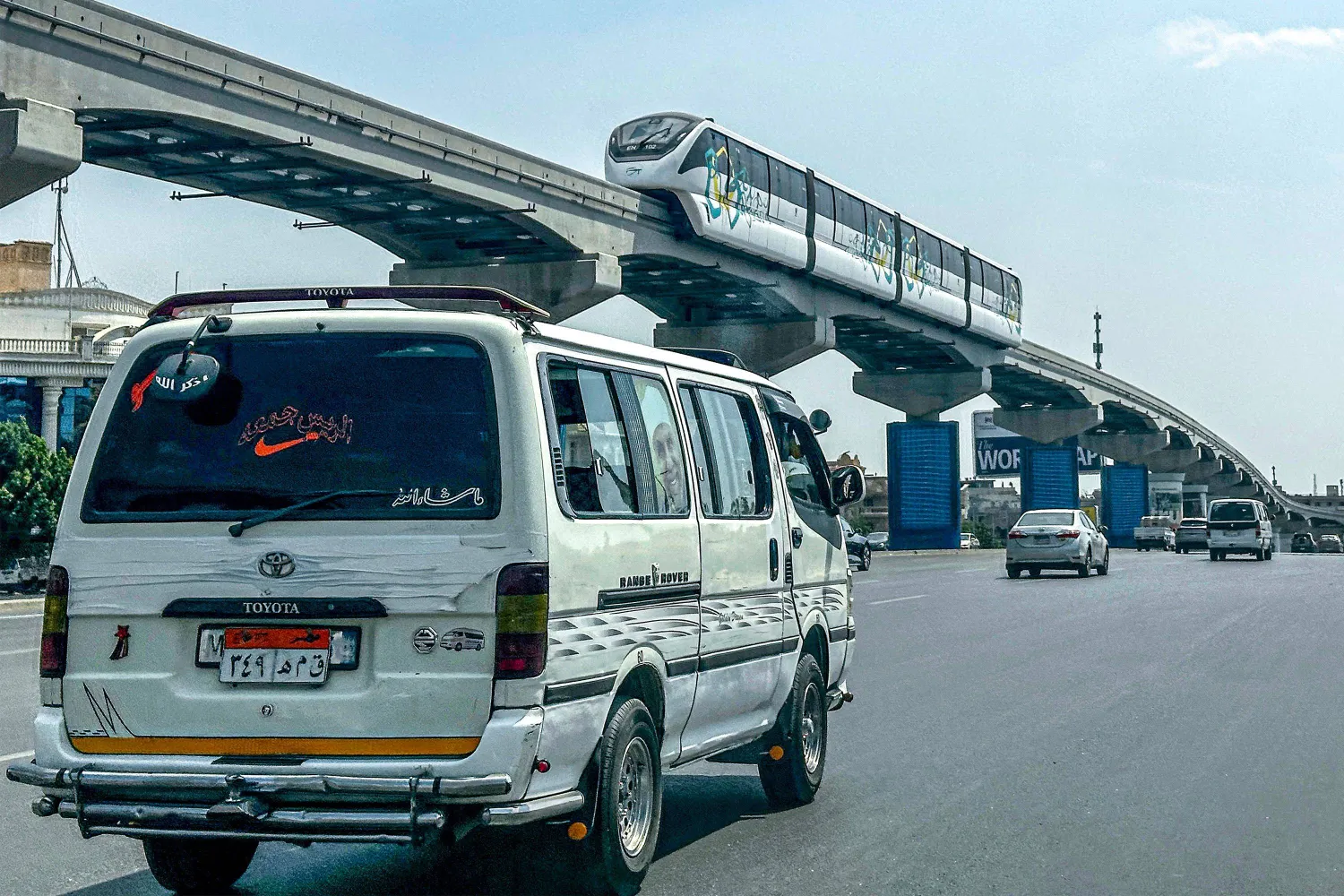 A minibus moves along a main road underneath new Cairo Monorail track as a train moves above in the Fifth Settlement, a neighborhood of the New Cairo suburb of Cairo, on May 22, 2026. (Photo by Khaled DESOUKI / AFP)