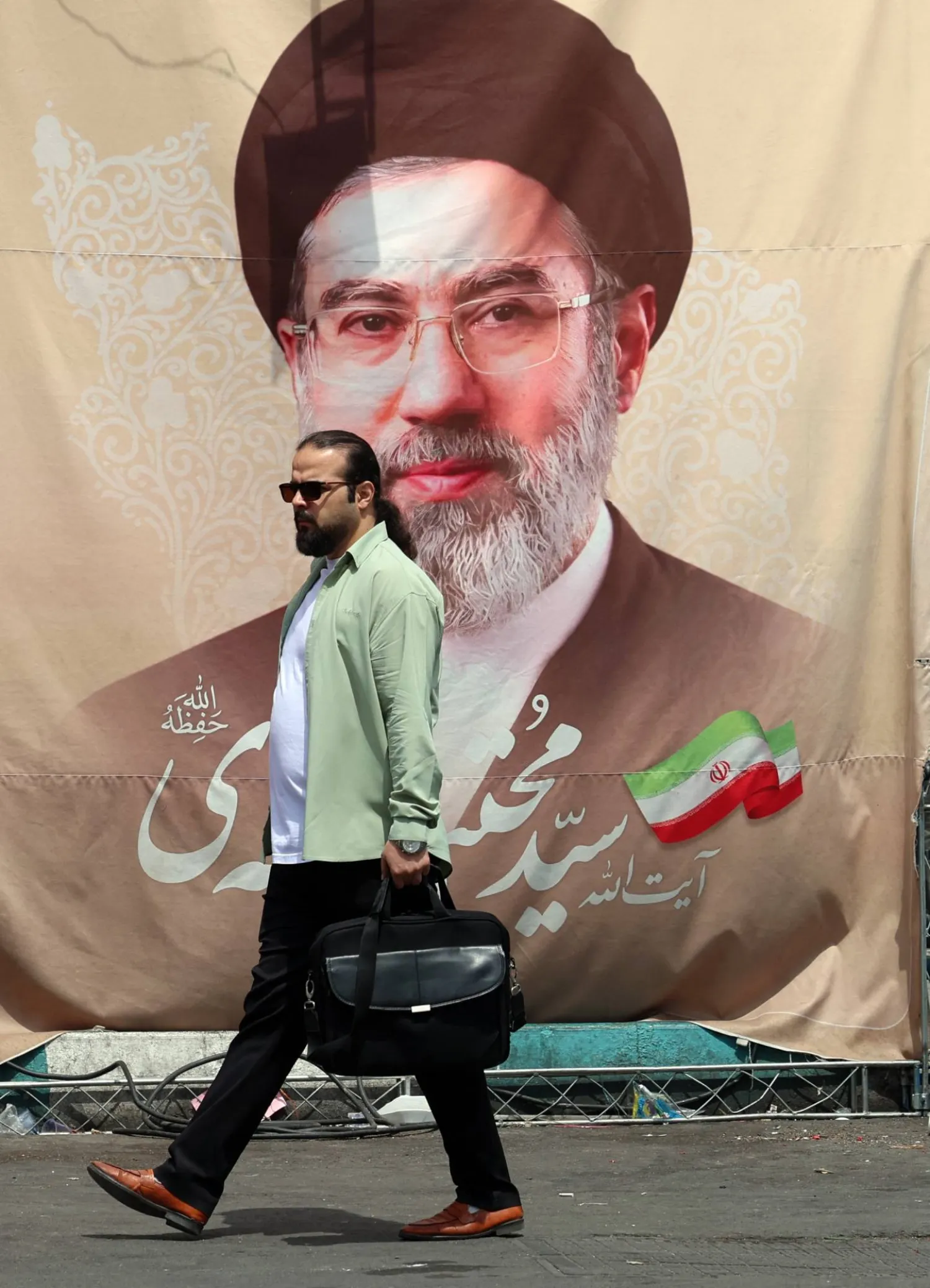 An Iranian man walks past a billboard carrying a picture of Iran' supreme leader Mojtaba Khamenei erected along a street in Tehran on May 28, 2026. (Photo by AFP) 