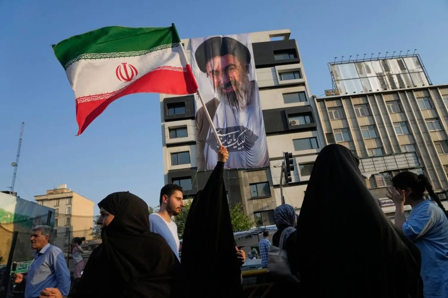 A woman holds up an Iranian flag in front of a banner showing a portrait of Supreme Leader Mojtaba Khamenei during a religious festival in Tehran, Iran, Thursday, June 4, 2026. (AP) 