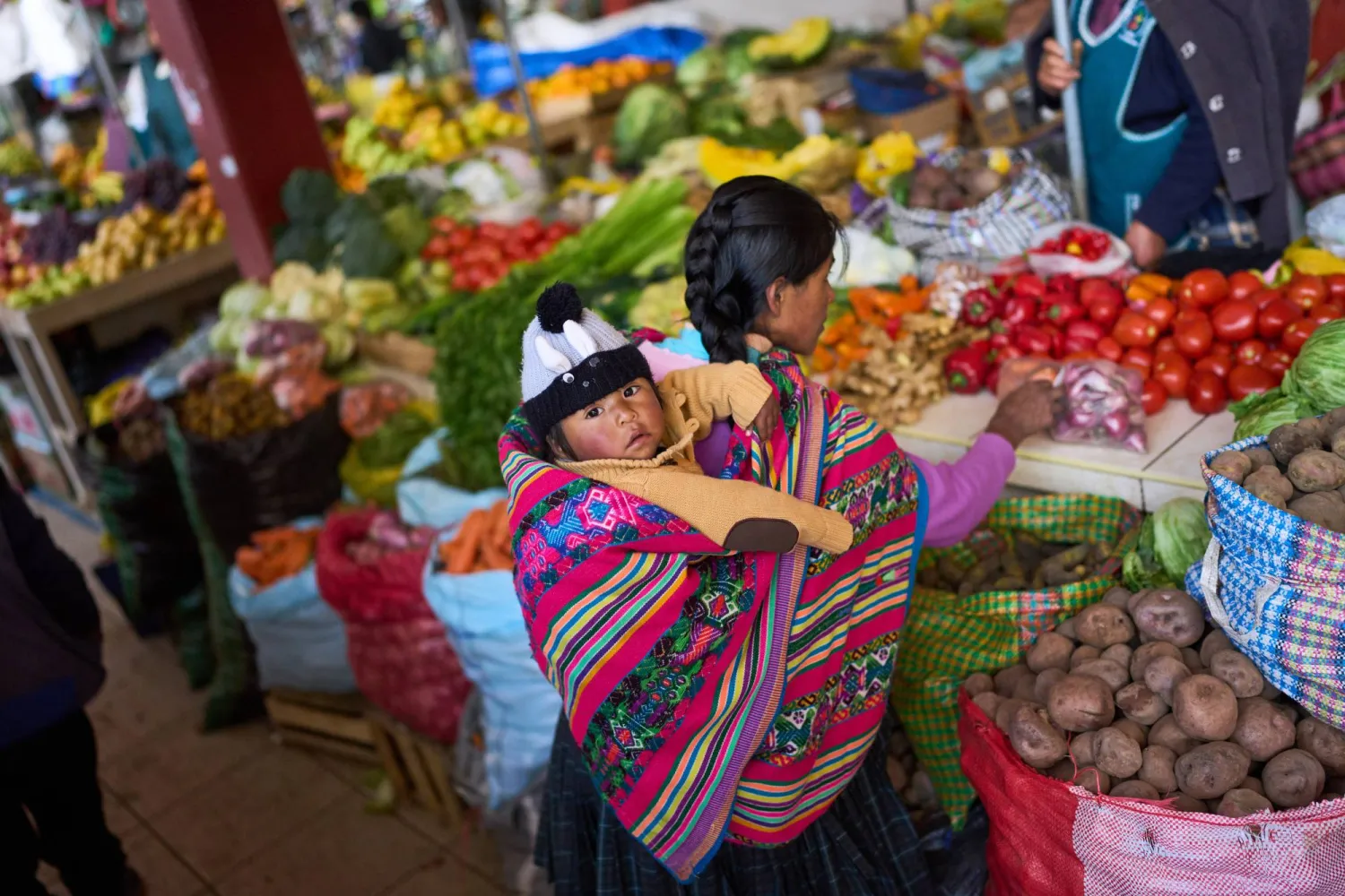 A shopper buys vegetables with her son at a street market in Urcos, Peru, Tuesday, June 2, 2026. (AP Photo/Rodrigo Abd)