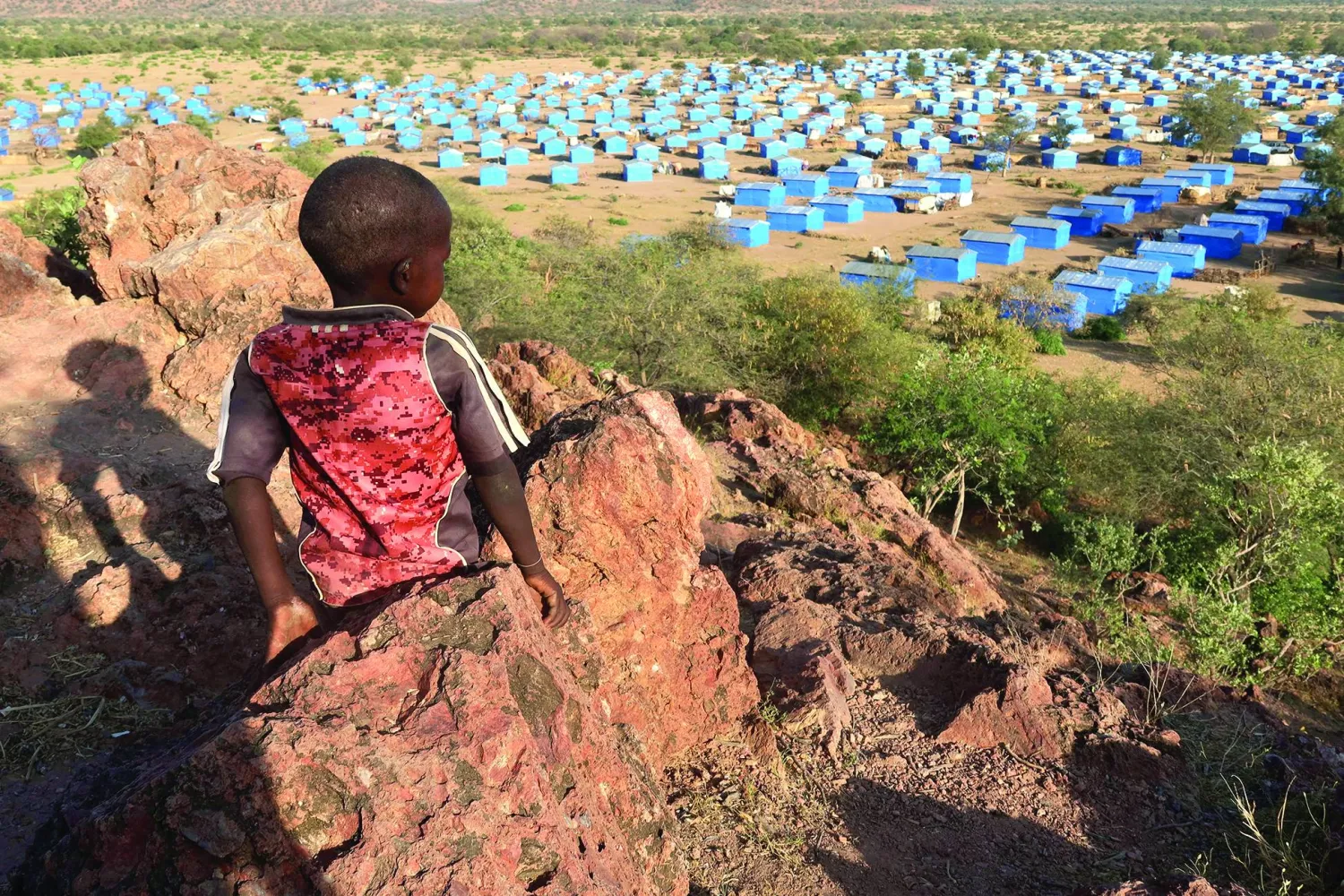 طفل يجلس على قمة تل مطل على مخيم للاجئين قرب الحدود السودانية مع تشاد في نوفمبر 2023 (رويترز)