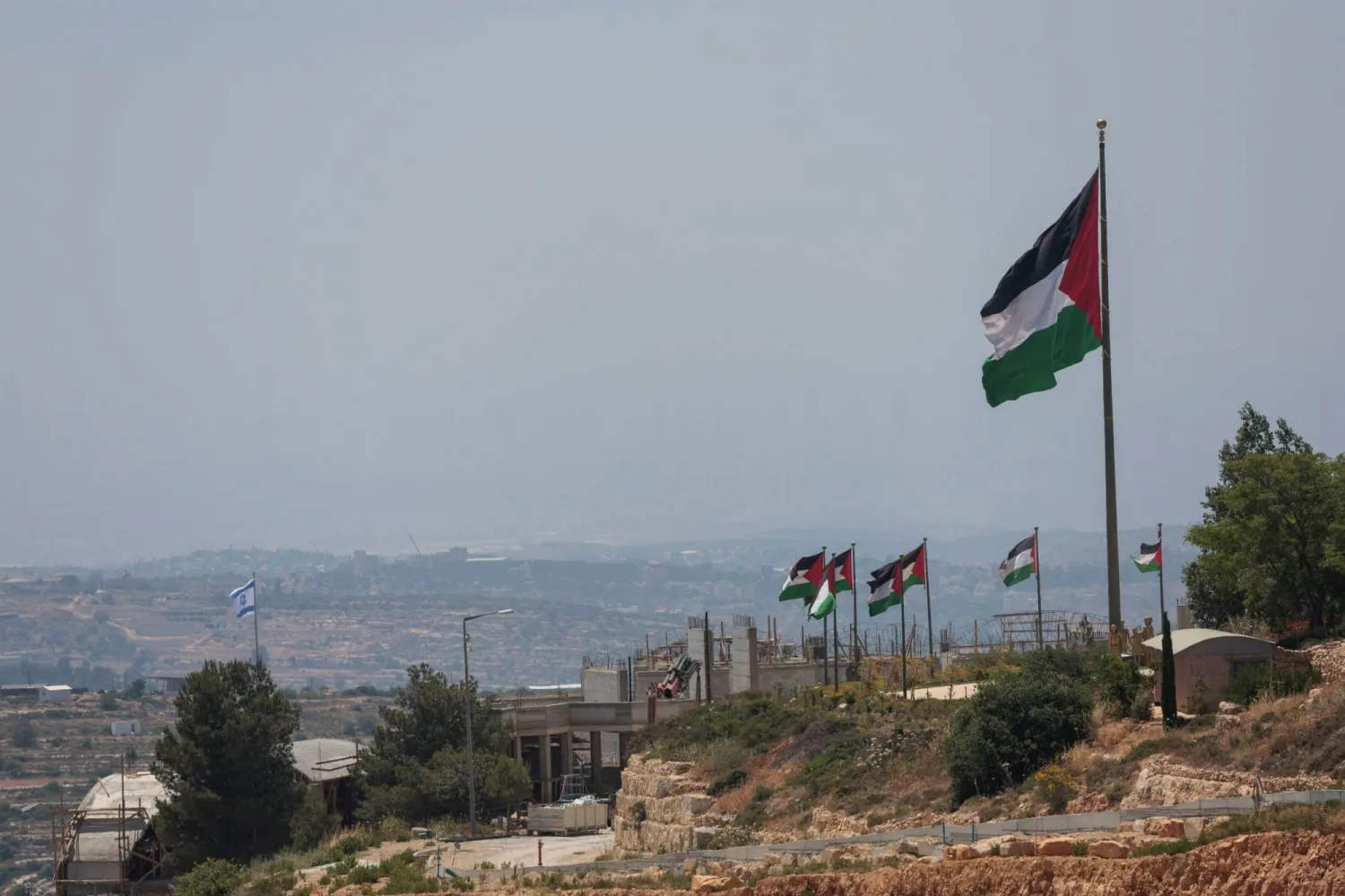 أعلام إسرائيلية ترفرف في مستوطنة إسرائيلية جديدة خلف أخرى فلسطينية قرب رام الله بالضفة الغربية (رويترز)