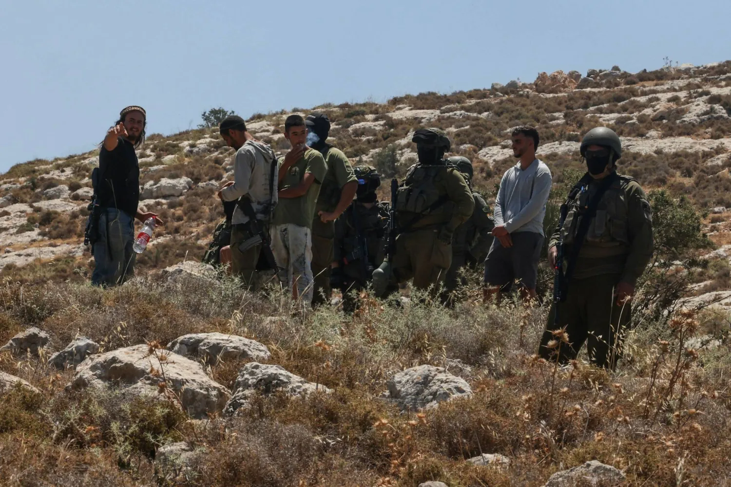 قوات إسرائيلية ومستوطنون مسلحون يقفون قبالة احتجاج لفلسطينيين على مصادرة أراضيهم قرب الخليل في الضفة الغربية المحتلة الثلاثاء (أ.ف.ب)