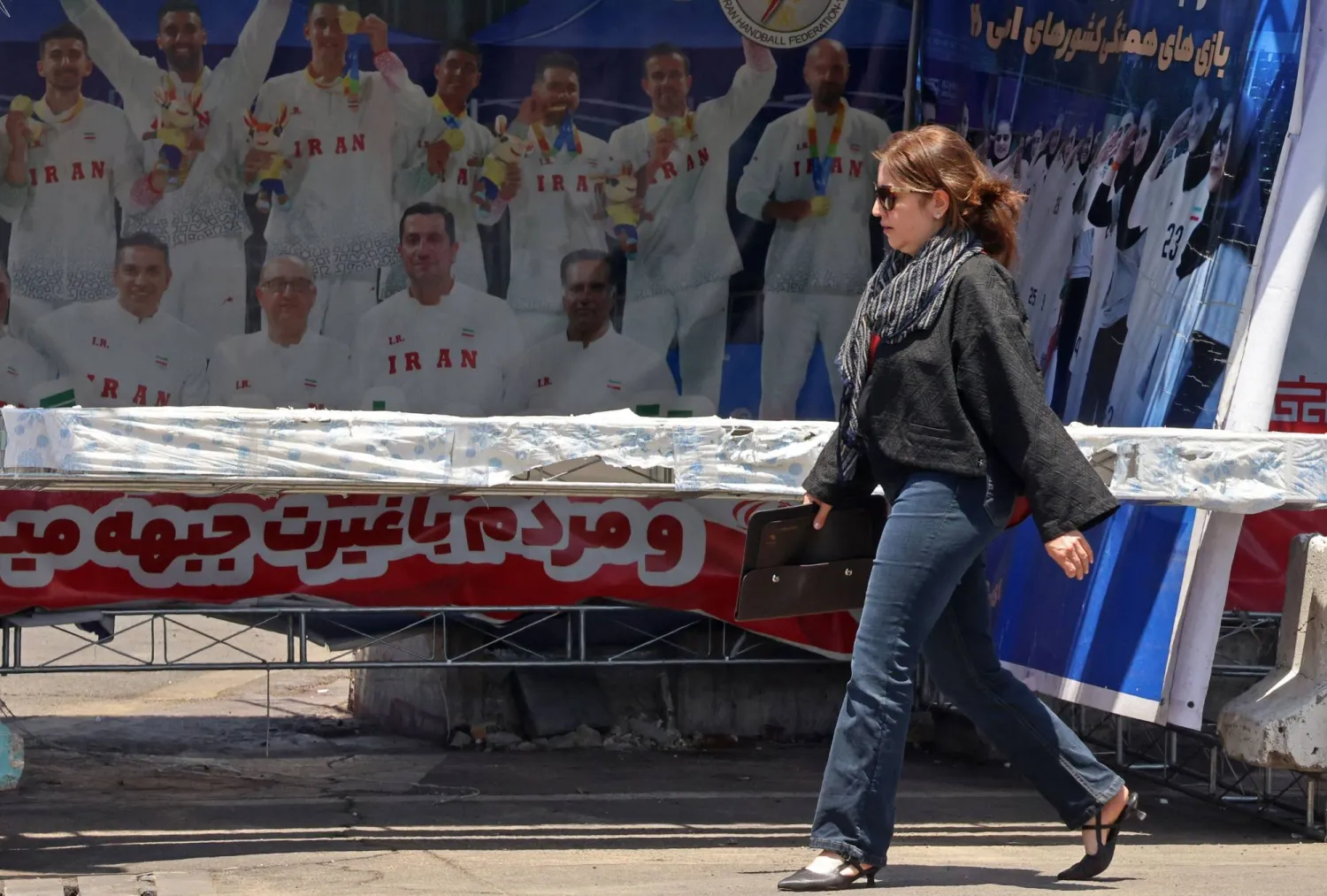 A woman walks past a banner bearing images of the members of Iranian national volleyball team, erected along a street at the Vanak Square in Tehran on June 10, 2026. (Photo by ATTA KENARE / AFP) 