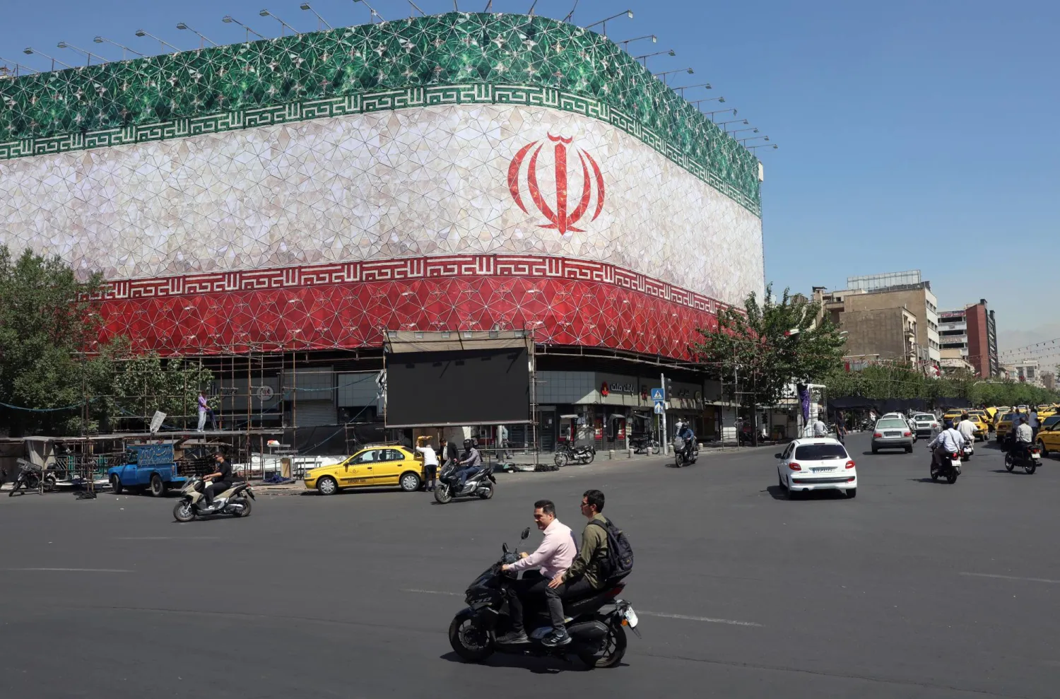 Iranians drive past a billboard featuring Iran's national flag at Enqelab Square in Tehran, Iran, 14 June 2026. EPA/ABEDIN TAHERKENAREH 